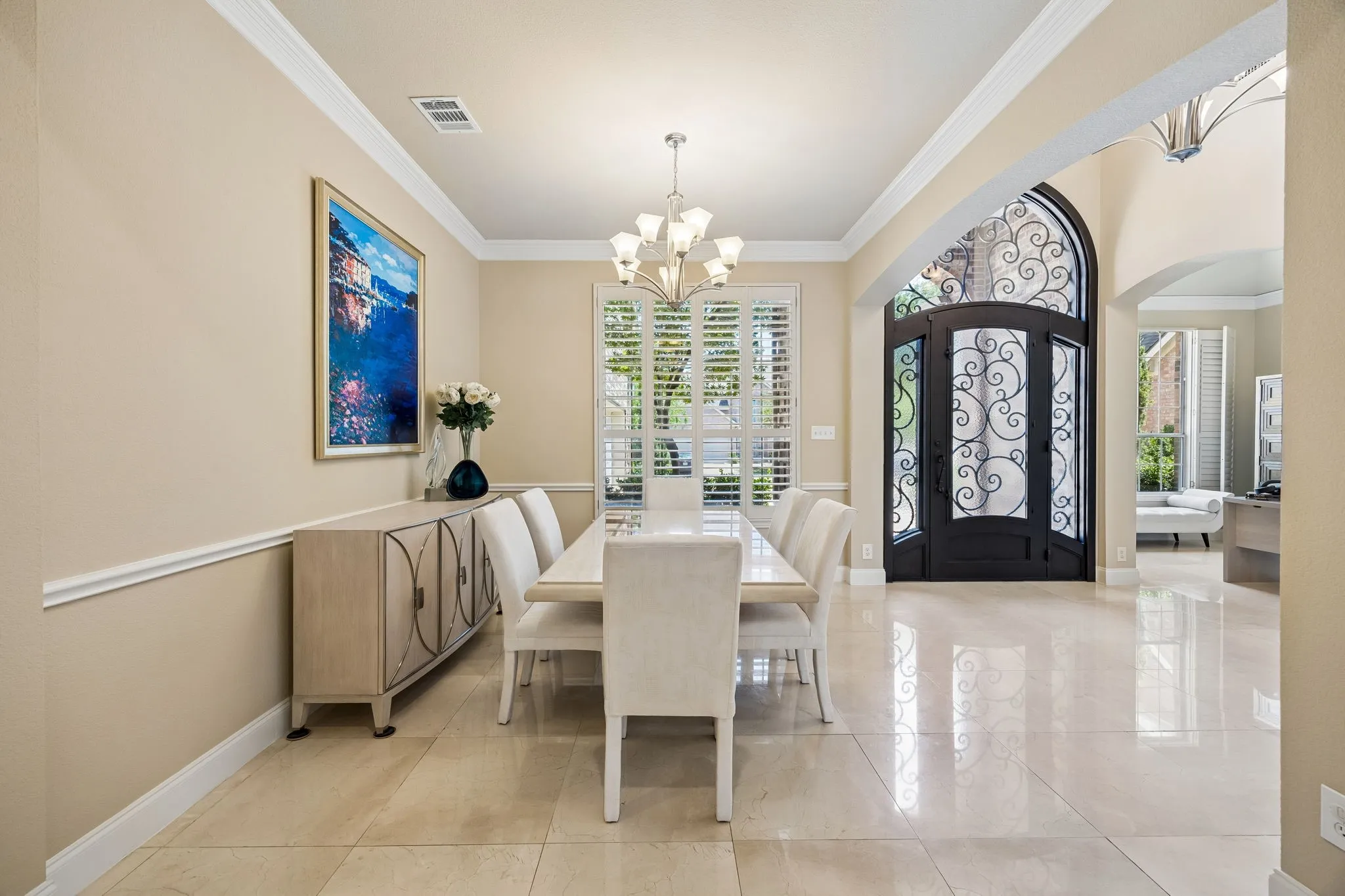 Elegant formal dining room showcases natural stone floors, detailed crown molding, and plantation shutters.  Positioned just off the grand entry, the open layout creates an inviting setting for intimate dinners or larger gatherings.