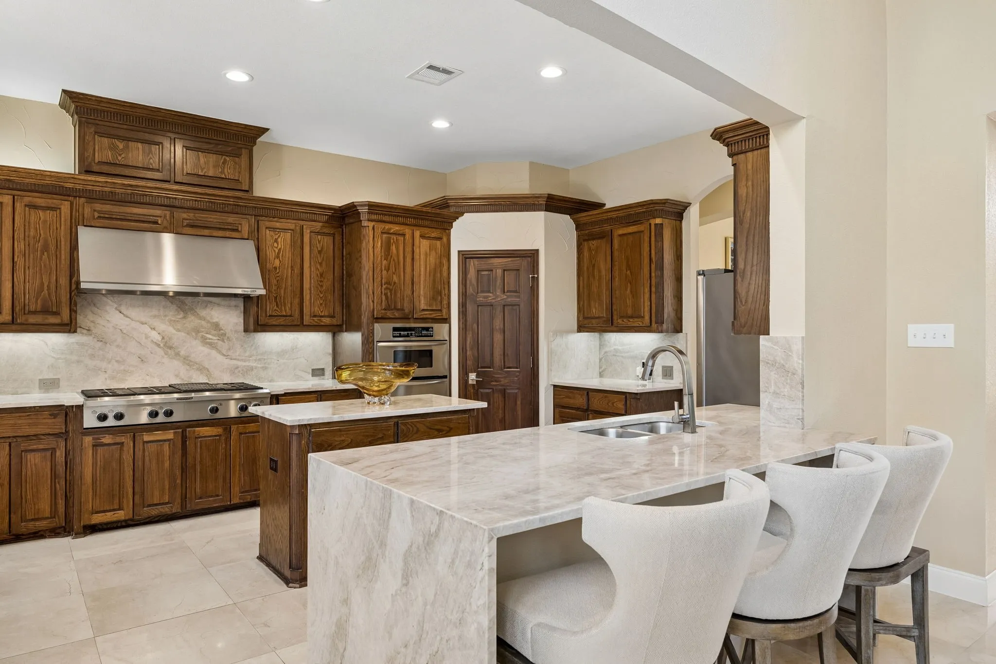 The beautifully updated kitchen showcases expansive Taj Mahal Quartzite countertops, and a striking waterfall edge peninsula.  This kitchen has multiple work surfaces and professional style cooking areas that provide space for meal preparation and gatherings. Sophisticated design with purpose.