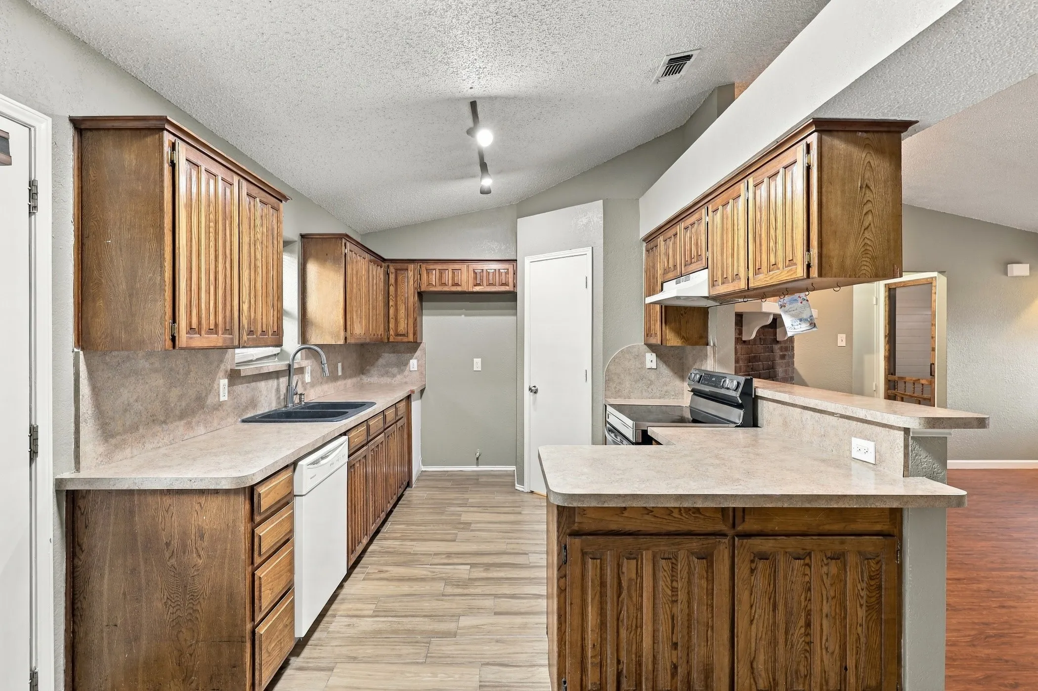 Kitchen featuring wood-finish cabinetry, light-toned countertops, a stainless steel sink, and wood-look flooring