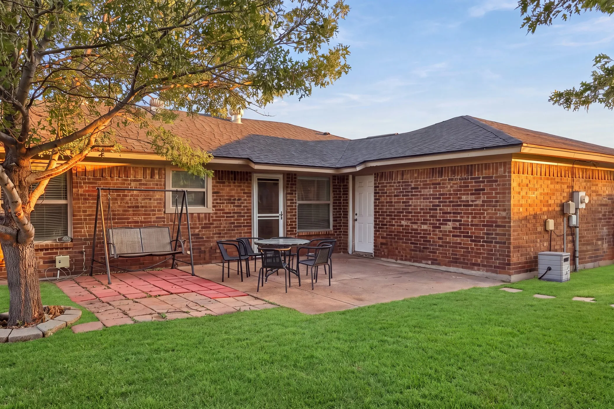 Brick exterior with a dark-shingle roof, offering a concrete patio, a paver area, and a large grassy yard