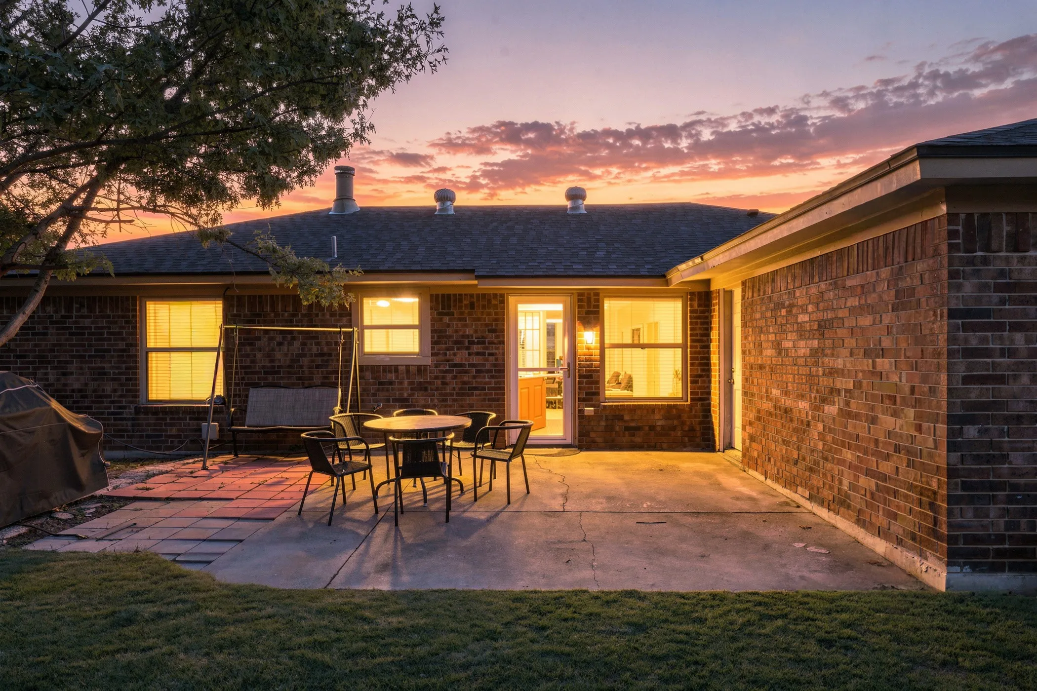 Brick exterior with a dark shingle roof, a concrete patio, and a grass lawn