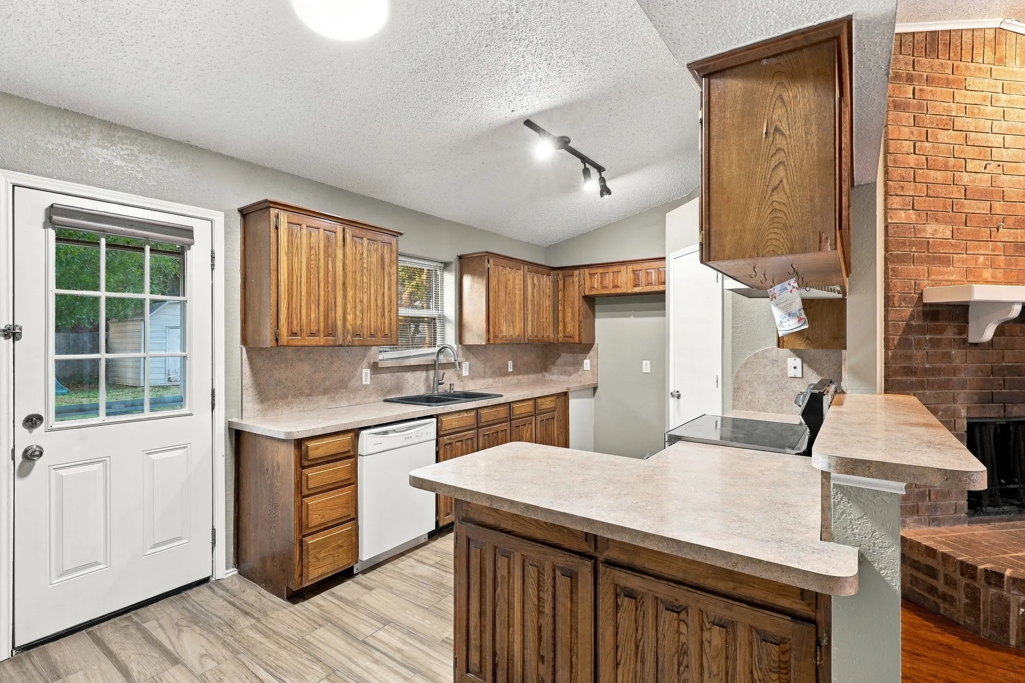 Kitchen featuring wood-finish cabinetry, light-toned countertops, a built-in dishwasher, and wood-finish flooring