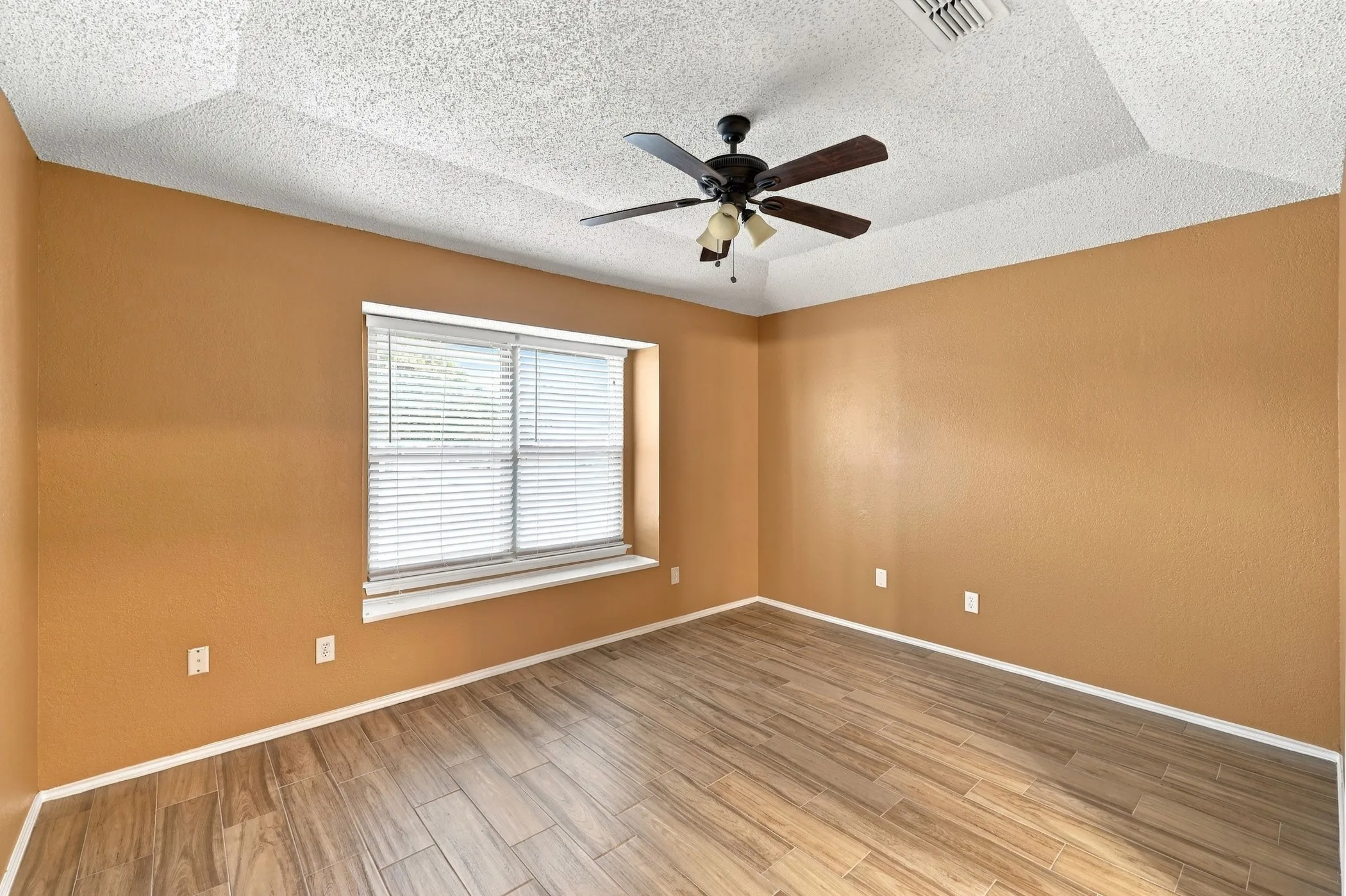 Tray ceiling with a ceiling fan, wood-finish flooring, and a large window with blinds