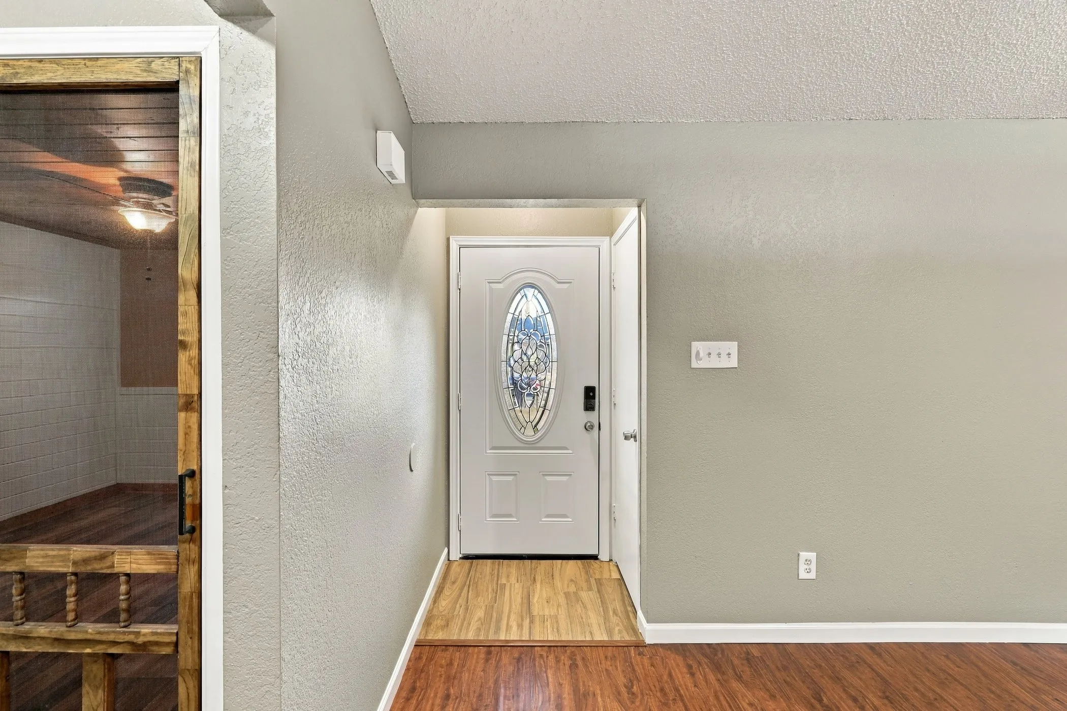 White entry door with decorative oval glass insert, wood-finish flooring, and light neutral wall paint