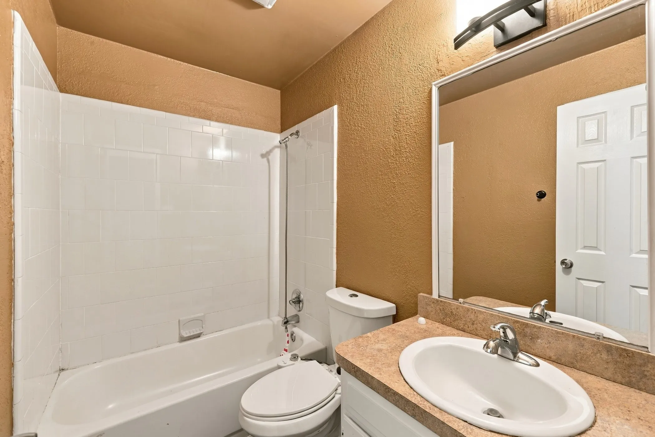 Integrated bathtub and shower with white tile surround, vanity with an oval sink and countertop, and a wall-mounted mirror
