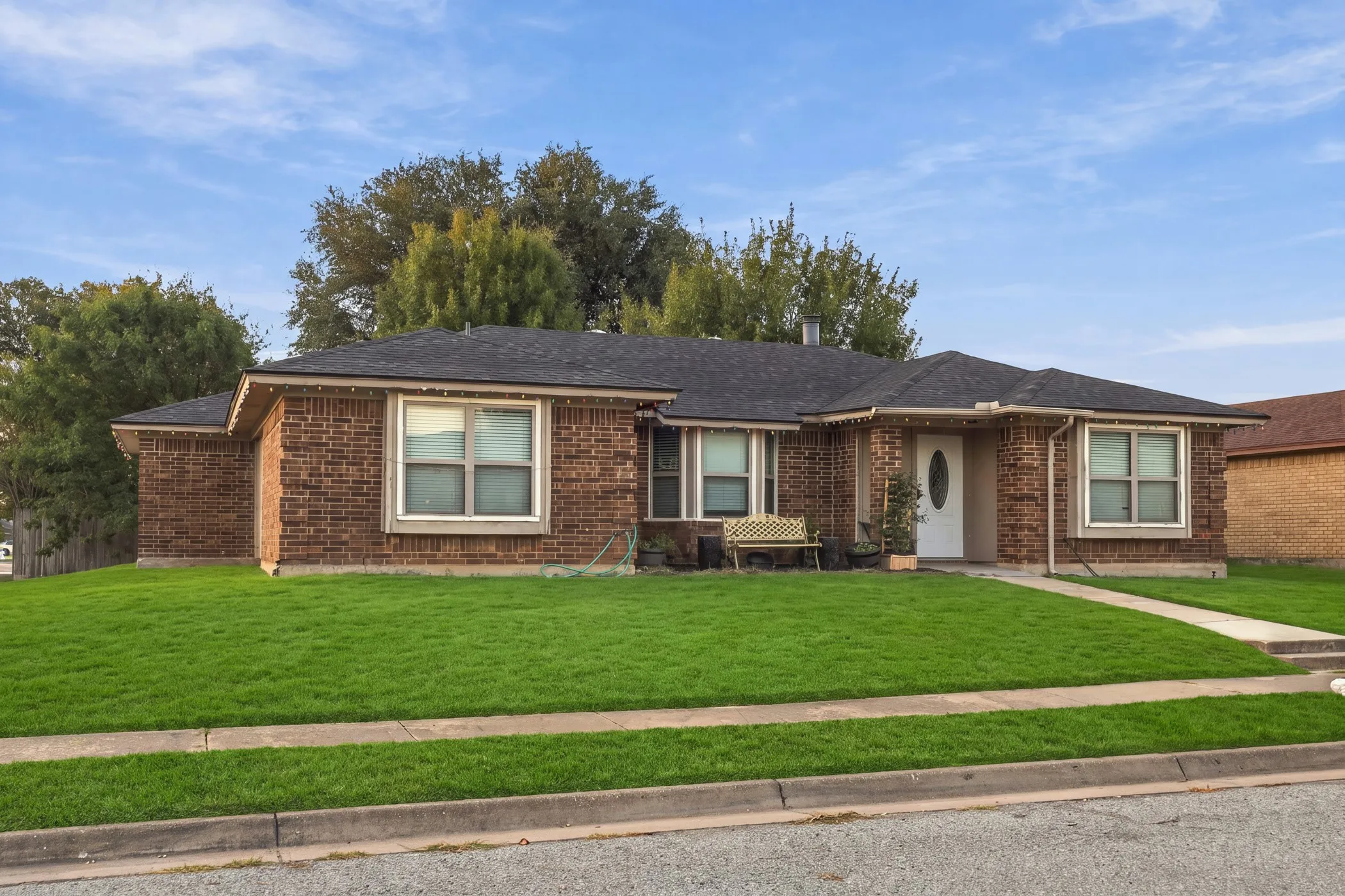 Brick exterior, dark shingle roof, white trim windows, white front door, concrete sidewalk