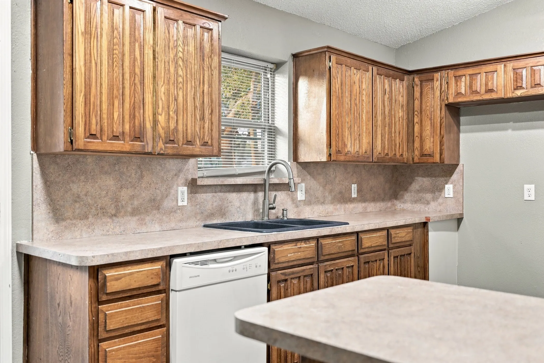 Kitchen featuring wood cabinetry, laminate countertops, a double basin sink with a high-arc faucet, and a built-in dishwasher