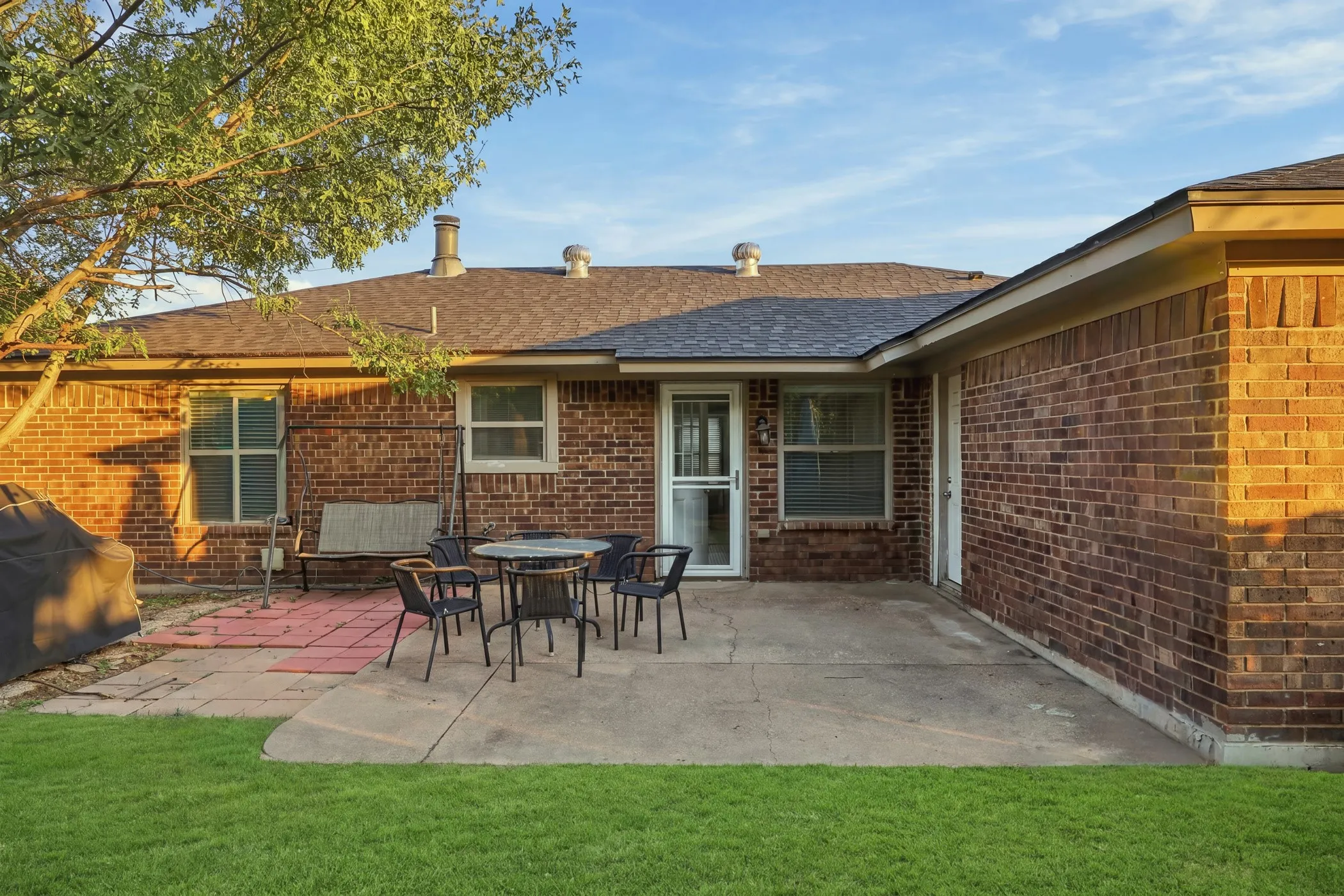 Brick exterior with a shingled roof, concrete patio, and a grass lawn