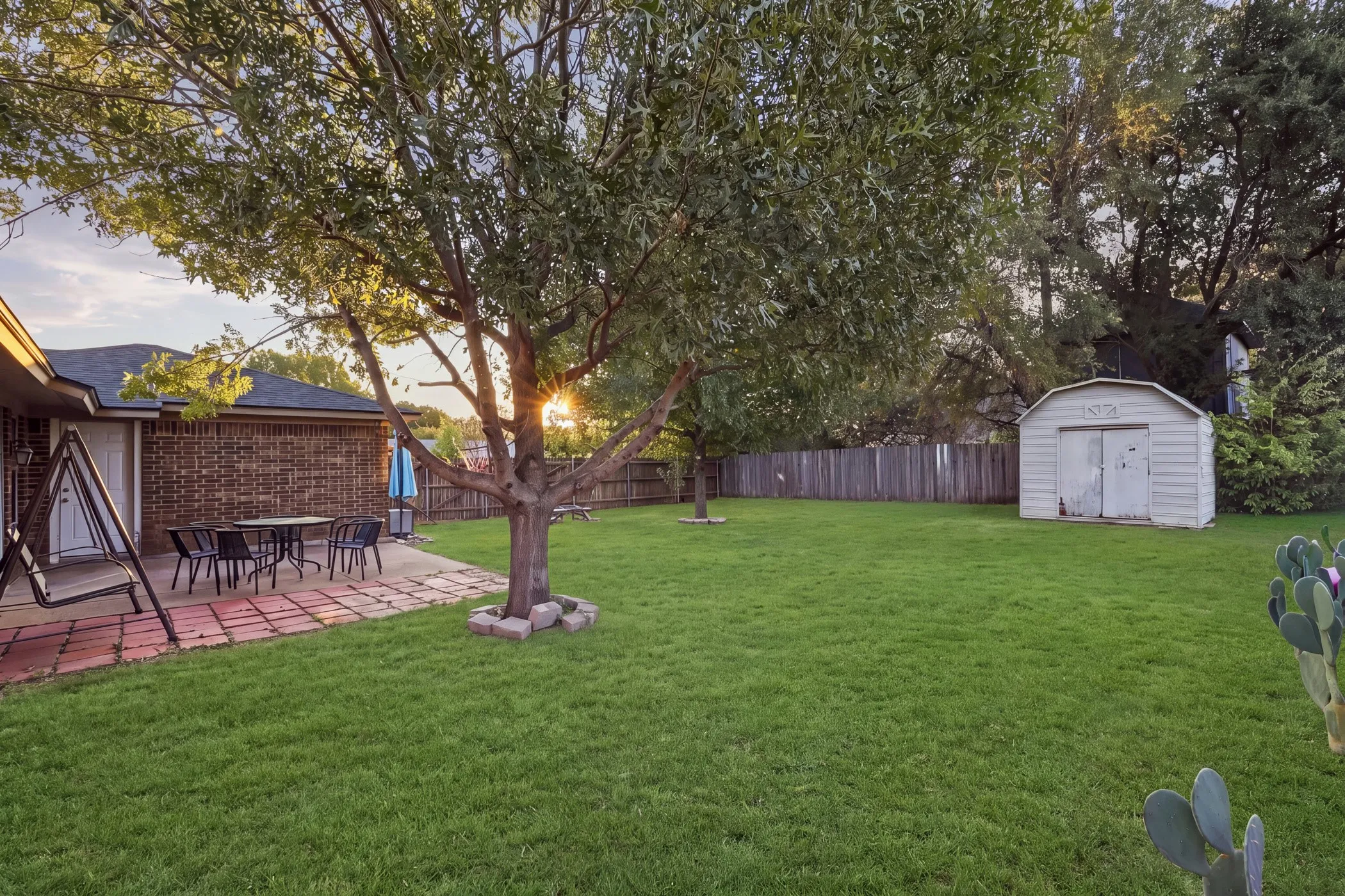 Expansive green lawn, mature trees, and a private patio with brick-finish pavers