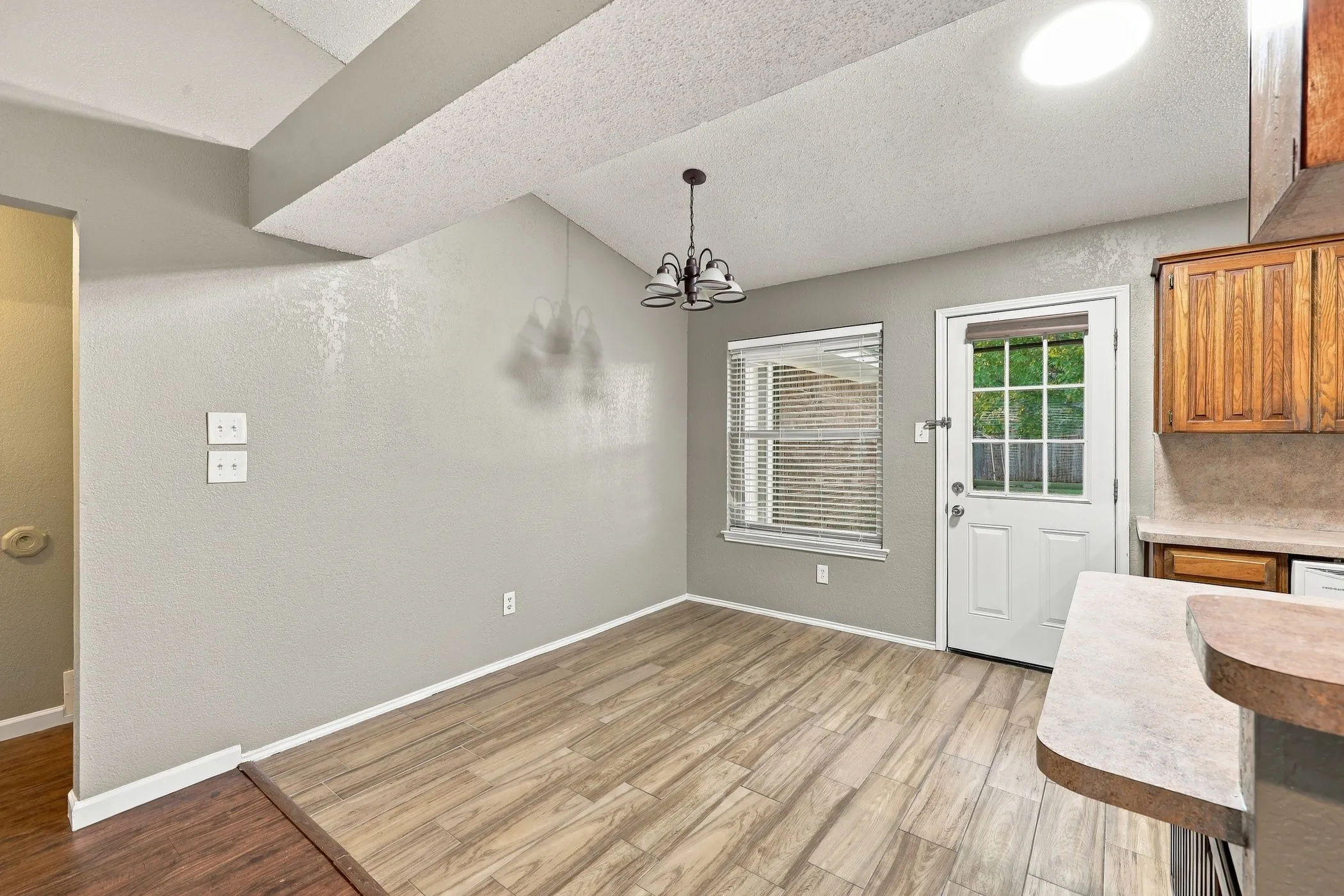 Angled ceiling with exposed beam, wood-finish flooring, kitchen cabinetry with built-in range hood, pendant lighting, and a skylight