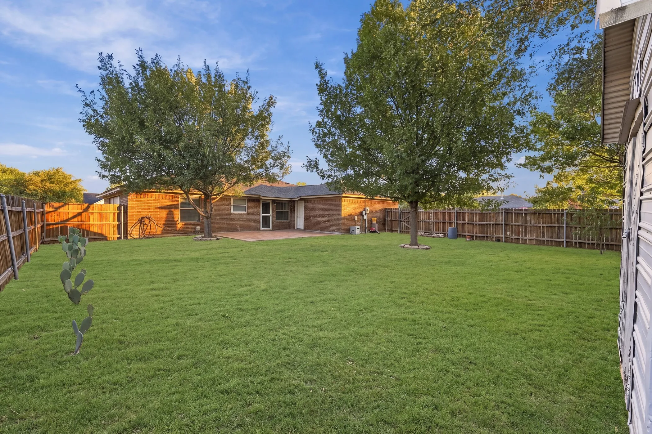 Expansive backyard with a manicured lawn, mature trees, and a brick exterior home