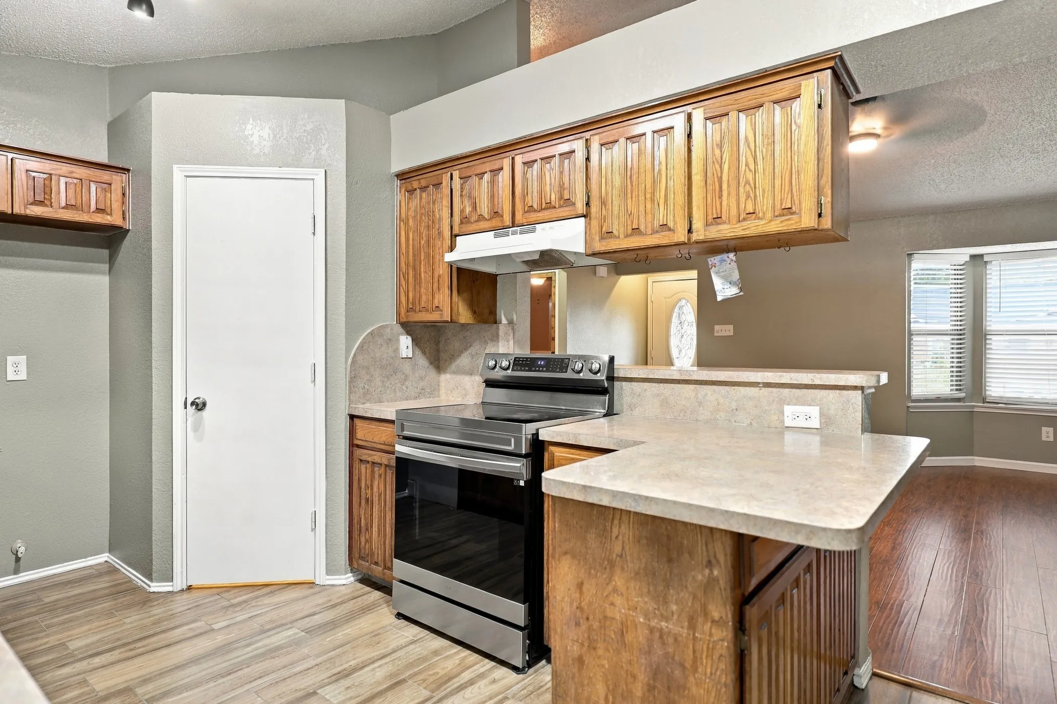 Wood-finish flooring, stainless steel range, and wood cabinetry with a light-toned countertop