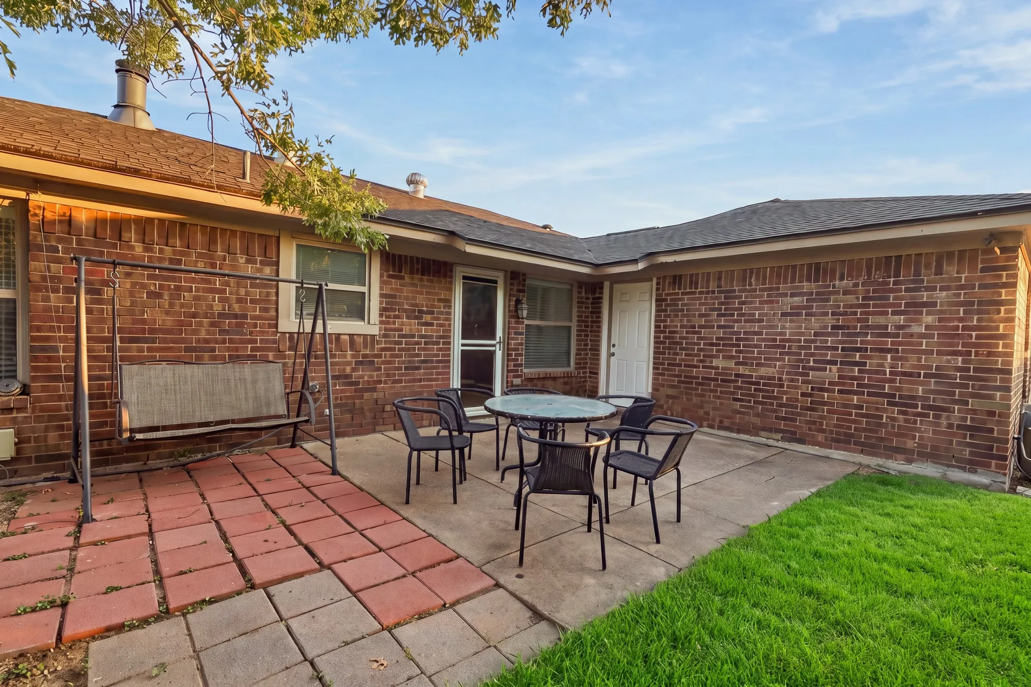 Brick exterior with multiple windows, a screened door, and a paved patio area