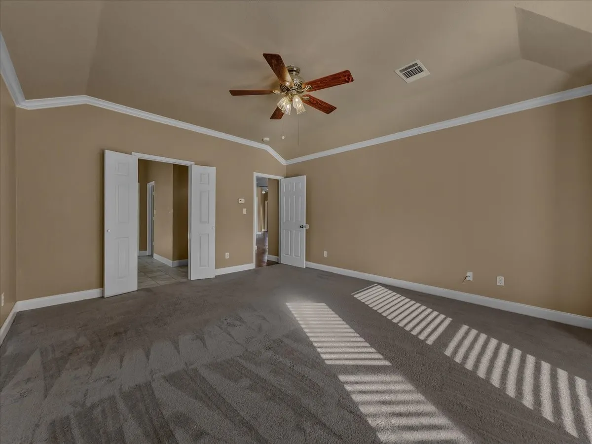 Vaulted ceiling with crown molding, ceiling fan, and carpeted flooring
