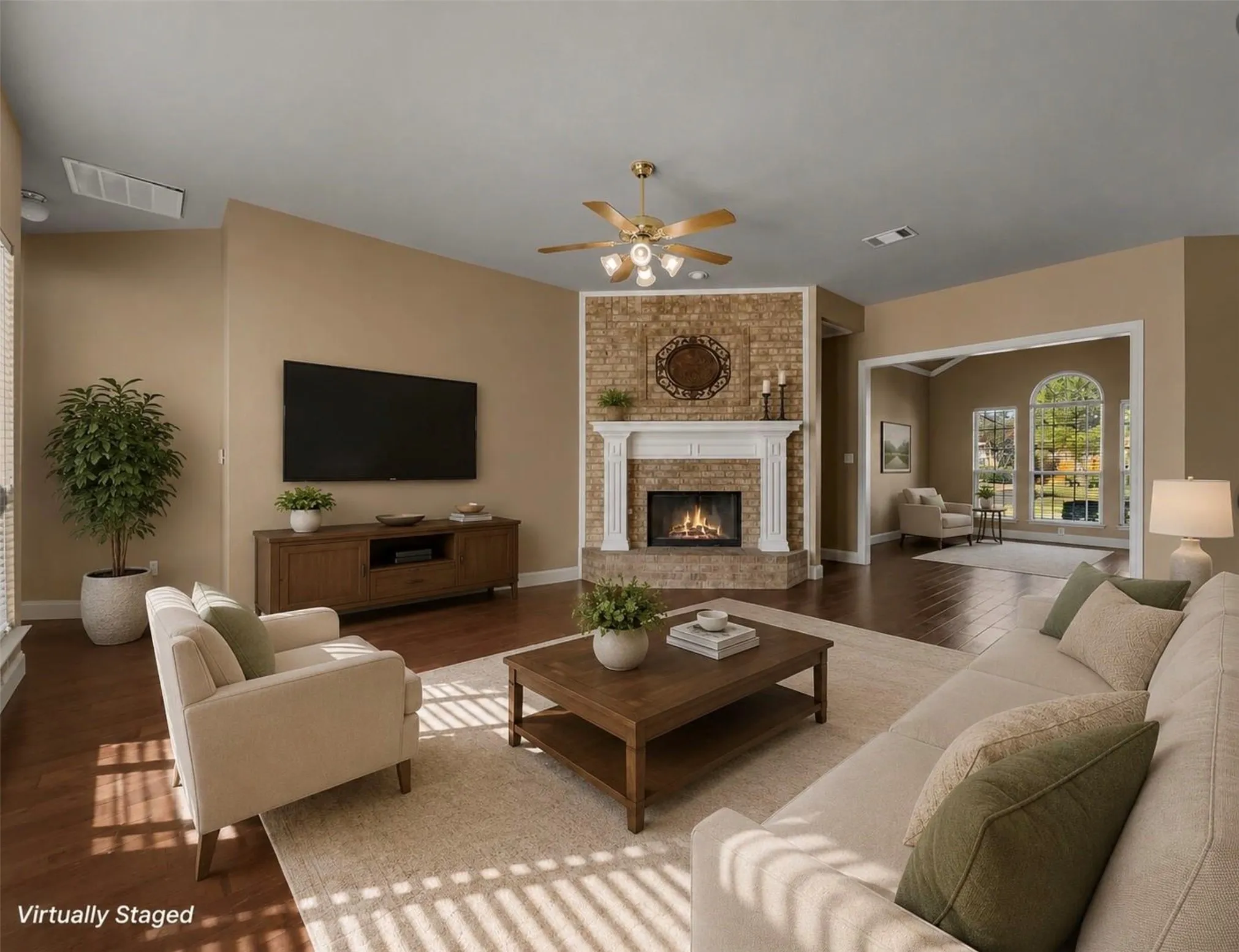 Spacious living area featuring wood-finish flooring, a brick fireplace with a white mantel, and a ceiling fan with integrated lighting