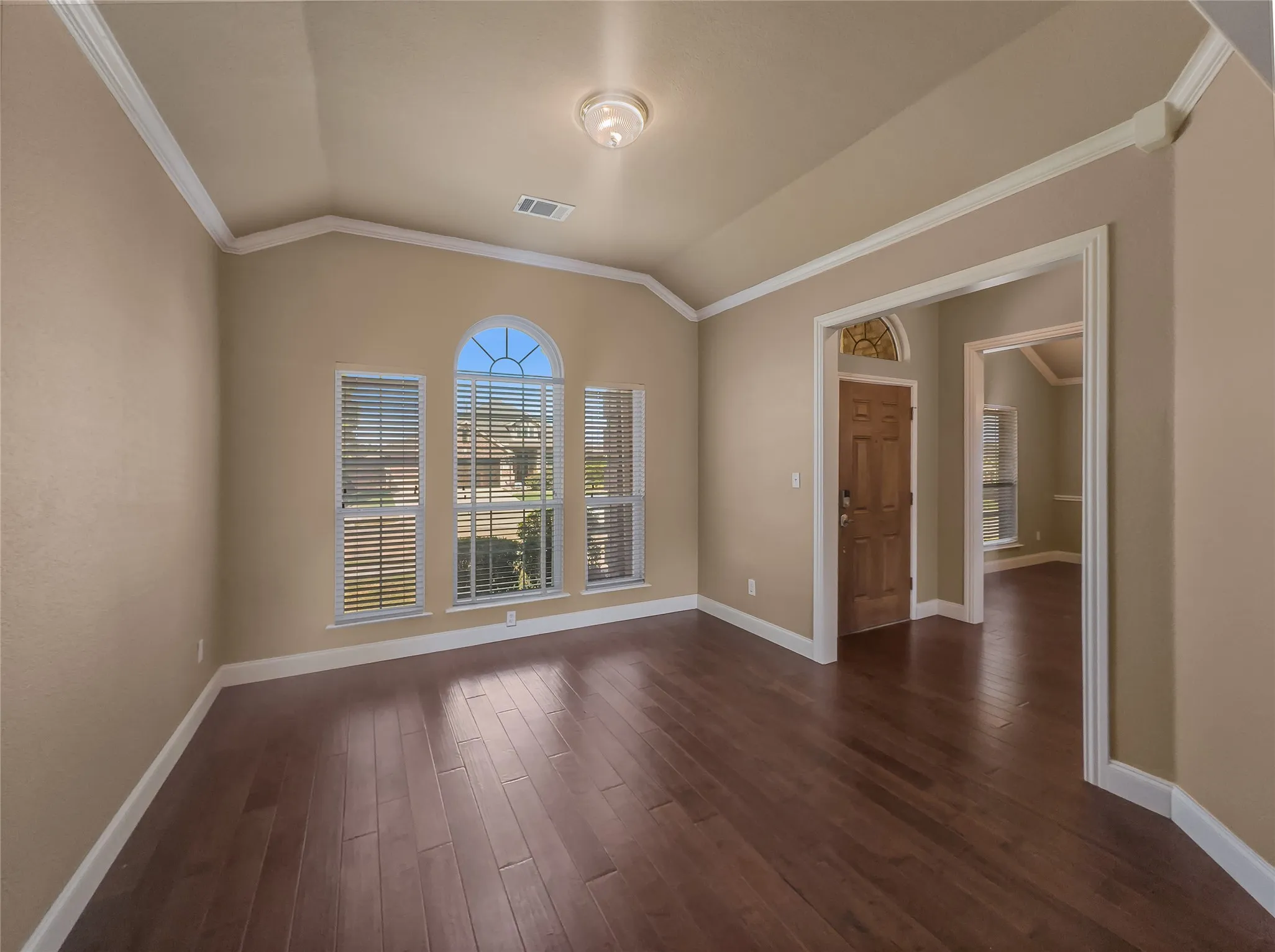 Vaulted ceiling with crown molding, wood-finish flooring, arched window, and paneled entry door