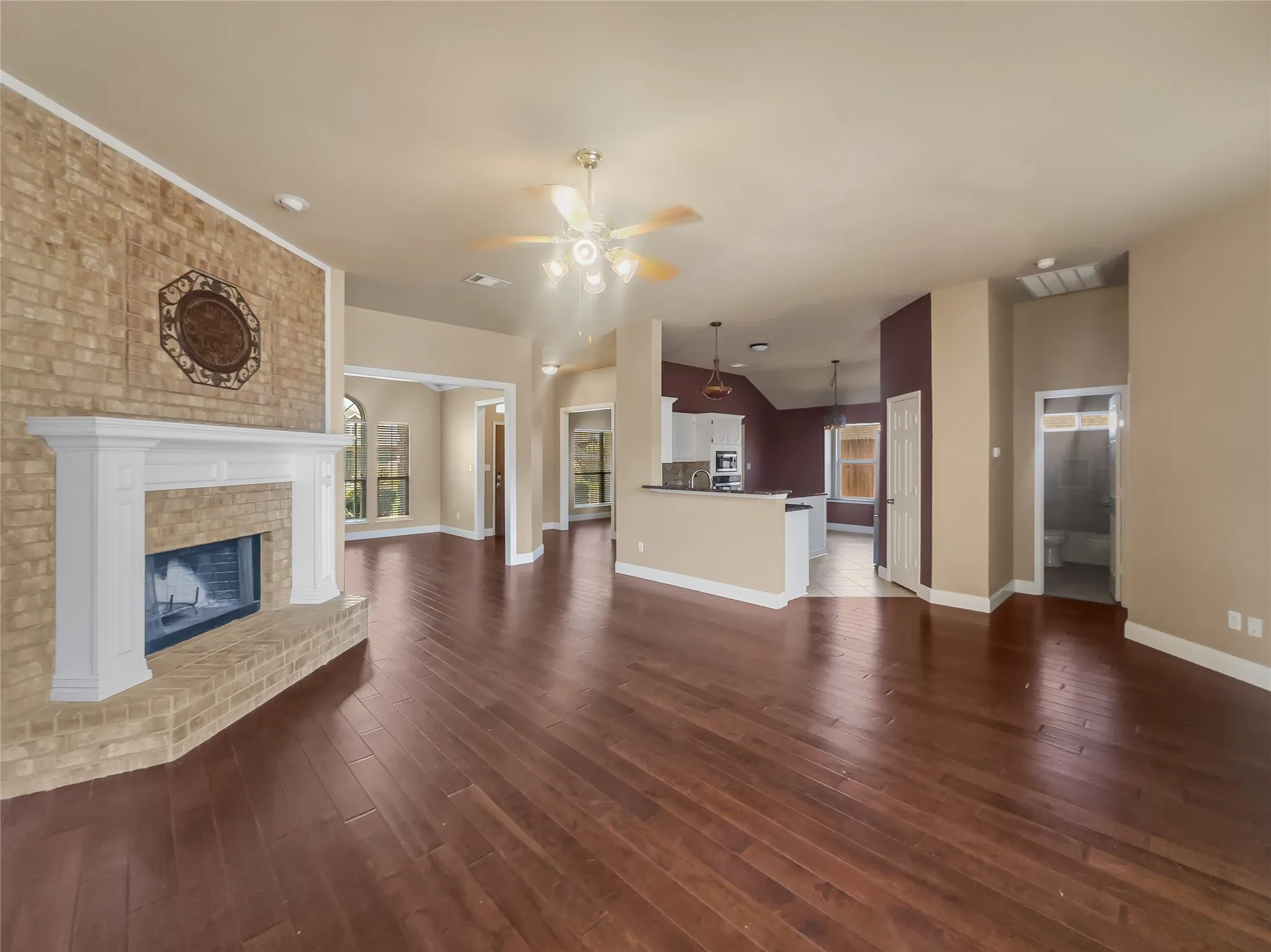 Expansive common area featuring wood-finish flooring, a brick fireplace with a white mantel, arched doorways, and recessed lighting