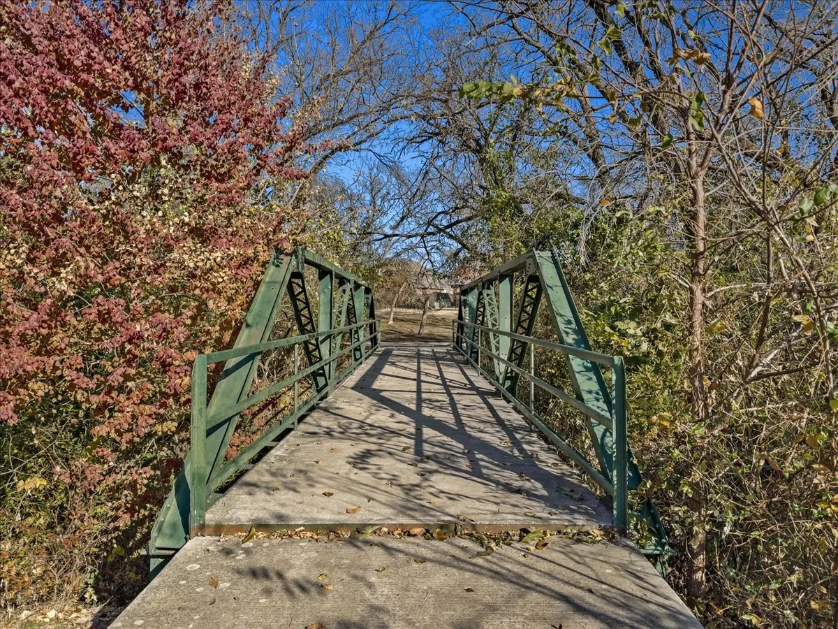 Concrete bridge with green metal truss railing, surrounded by mature trees with visible foliage