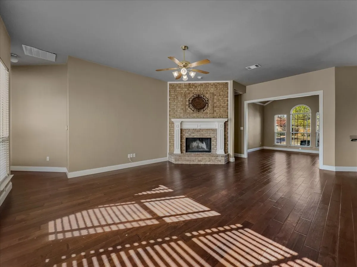 Brick-surround fireplace with a white mantel, rich wood-finish flooring, and arched windows