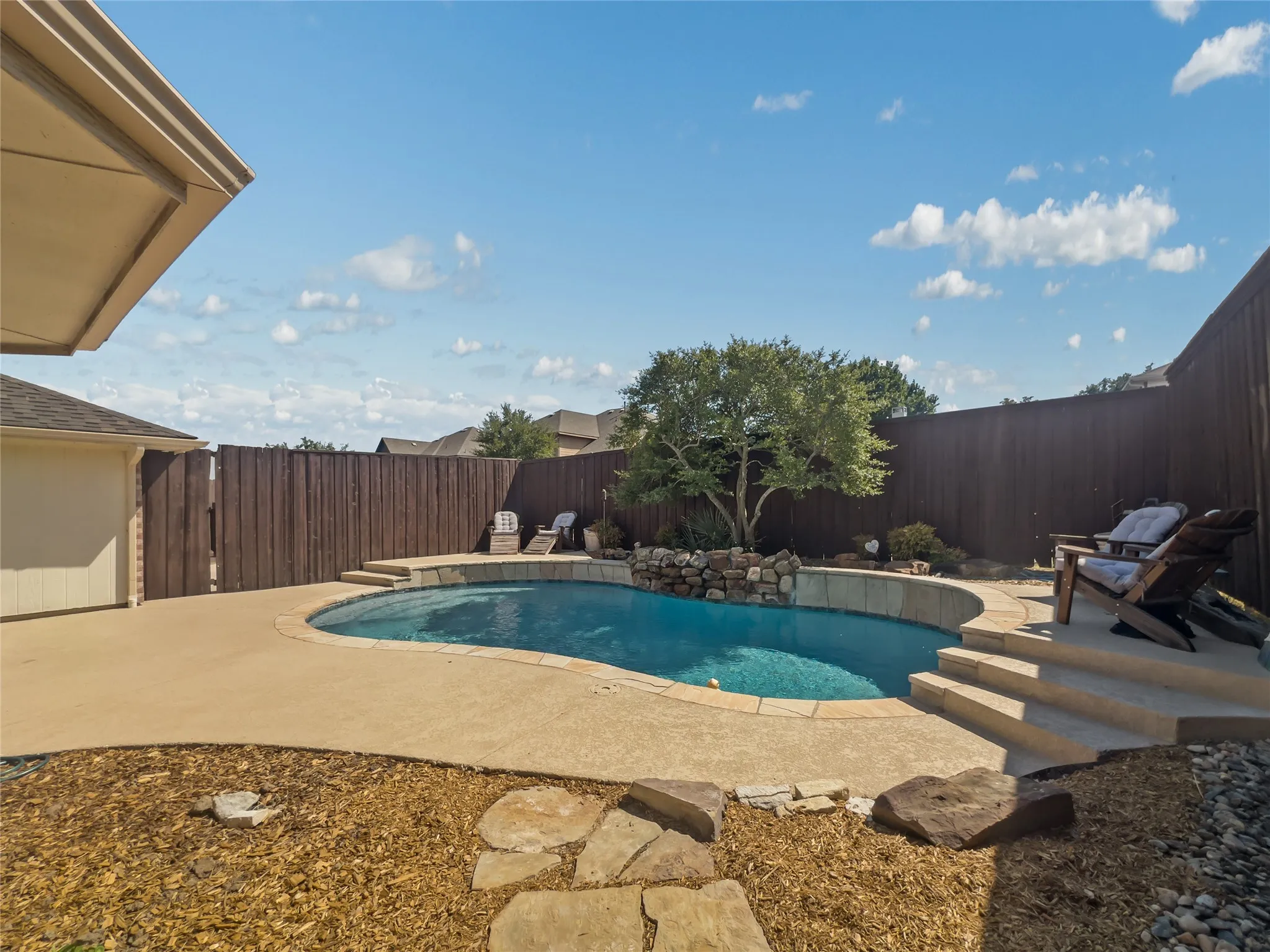 Resort-style pool with a rock waterfall feature, concrete decking, and integrated steps