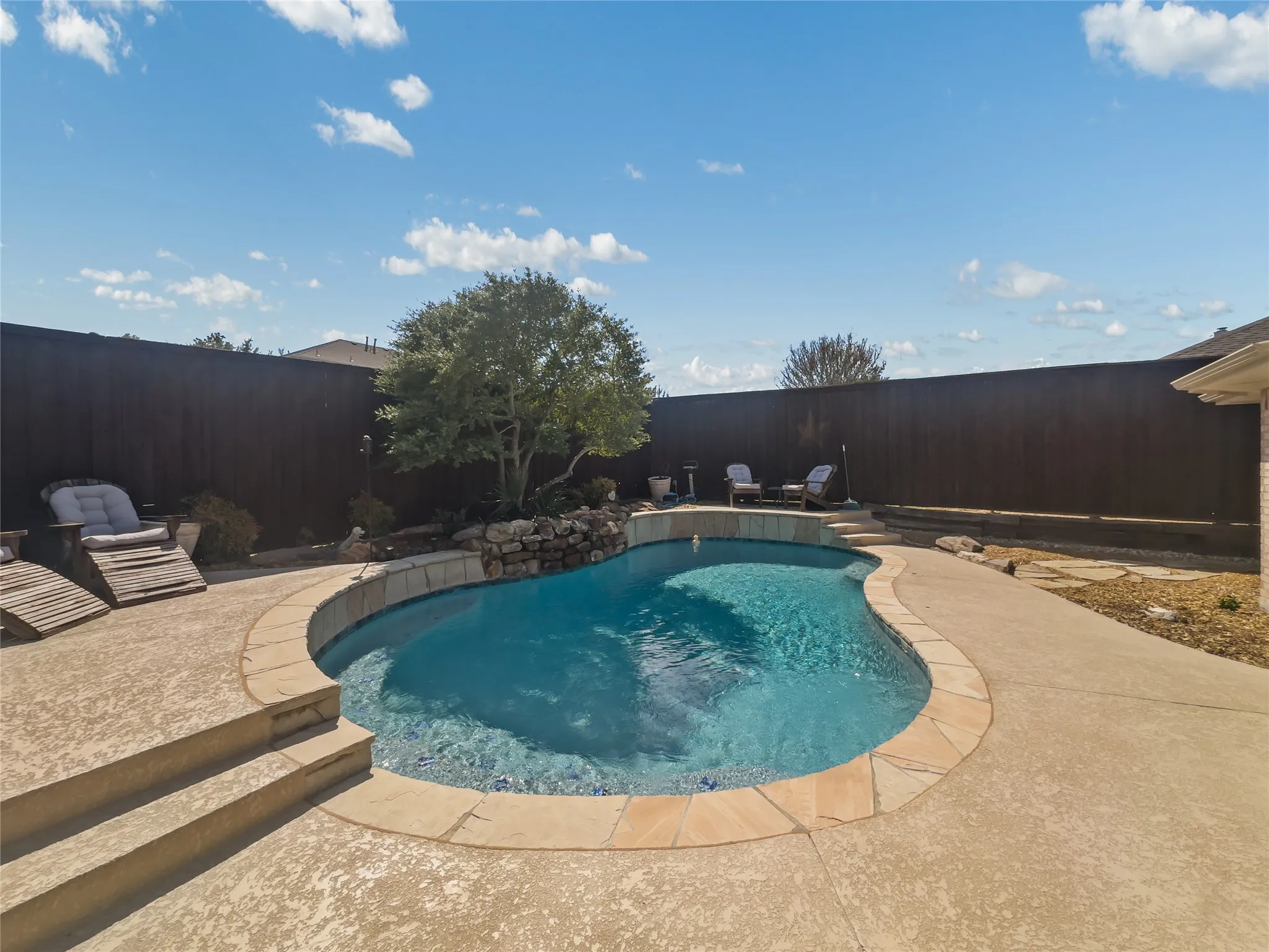 Custom-shaped pool with stone coping, a rock water feature, and surrounding concrete decking