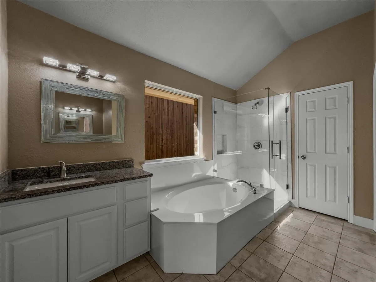 Vaulted ceiling bathroom featuring a glass-enclosed shower with tiled walls, a separate built-in soaking tub, a vanity with a granite countertop, and a single-basin sink