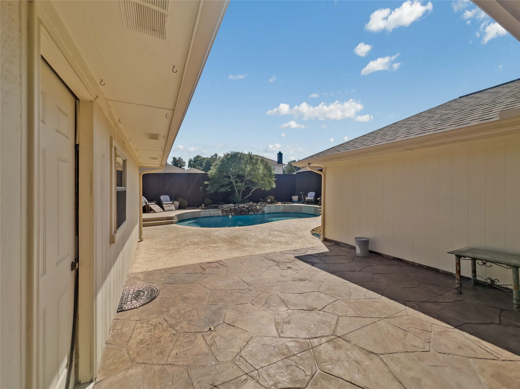 Expansive stamped concrete patio with an irregular pattern, leading to a curved in-ground pool