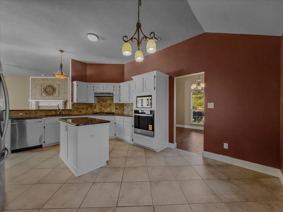 Kitchen featuring white cabinetry, a center island, built-in stainless steel appliances, tile flooring, and stone countertops