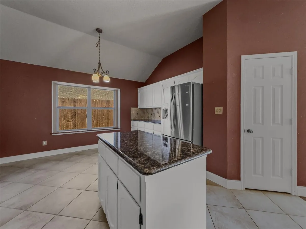 Kitchen island with stone-finish countertop, white cabinetry, and stainless steel refrigerator