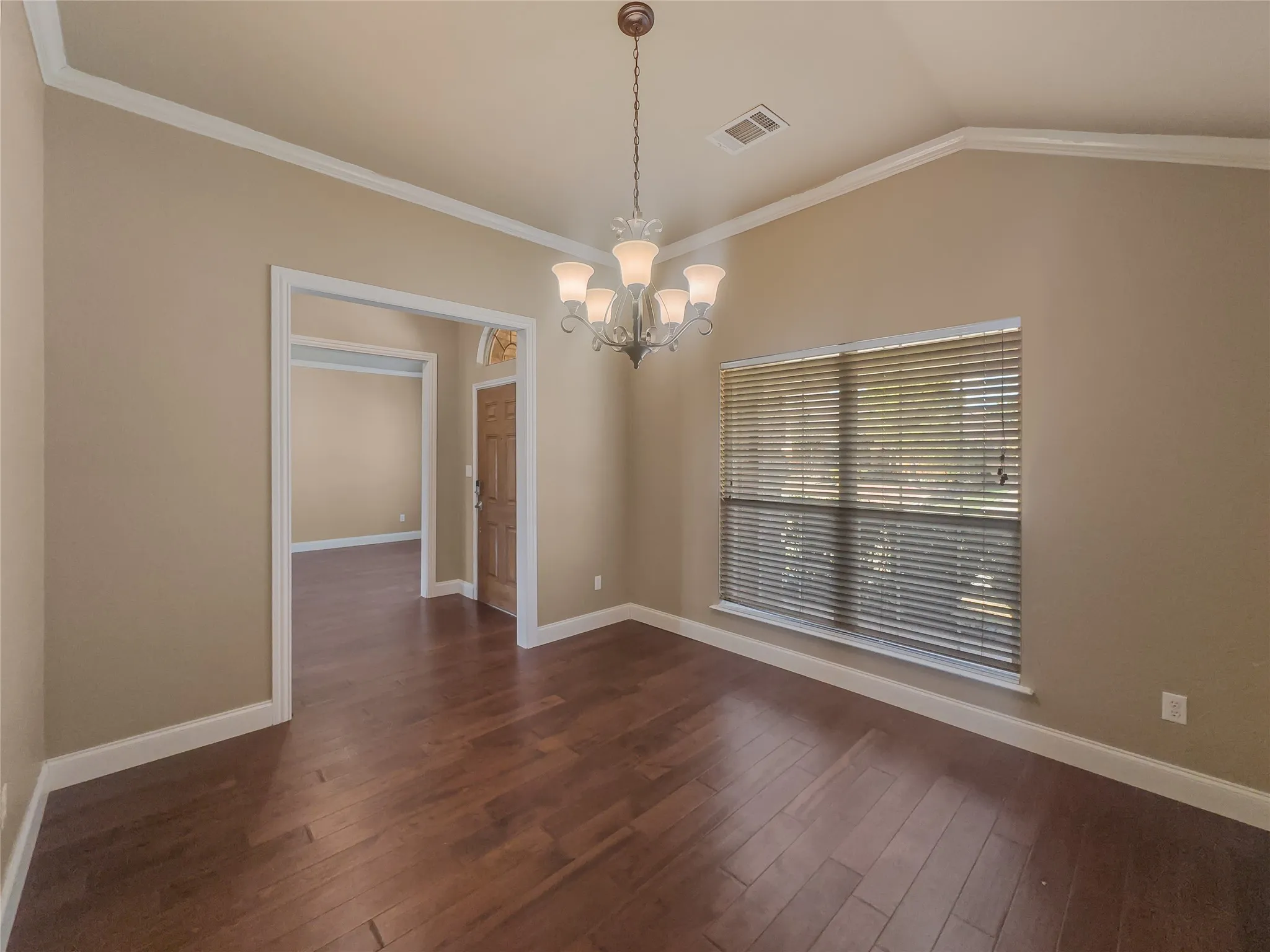 Wood-finish flooring, vaulted ceiling, crown molding, built-in lighting fixture, and a window with blinds