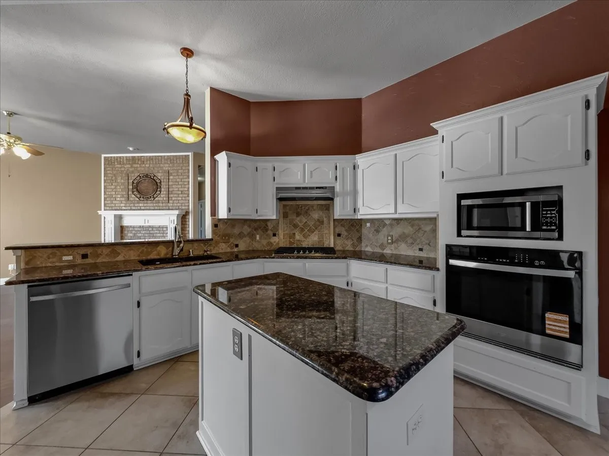 Kitchen featuring white cabinetry, dark stone countertops, tile backsplash, stainless steel appliances, and a central island