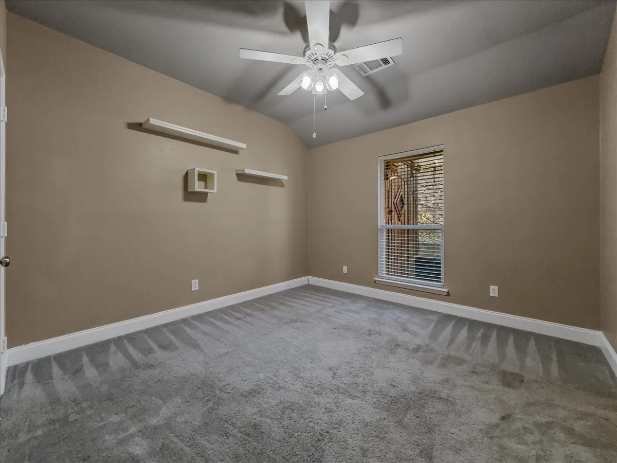 Vaulted ceiling featuring a ceiling fan with integrated lighting, window with horizontal blinds, and gray carpeted flooring
