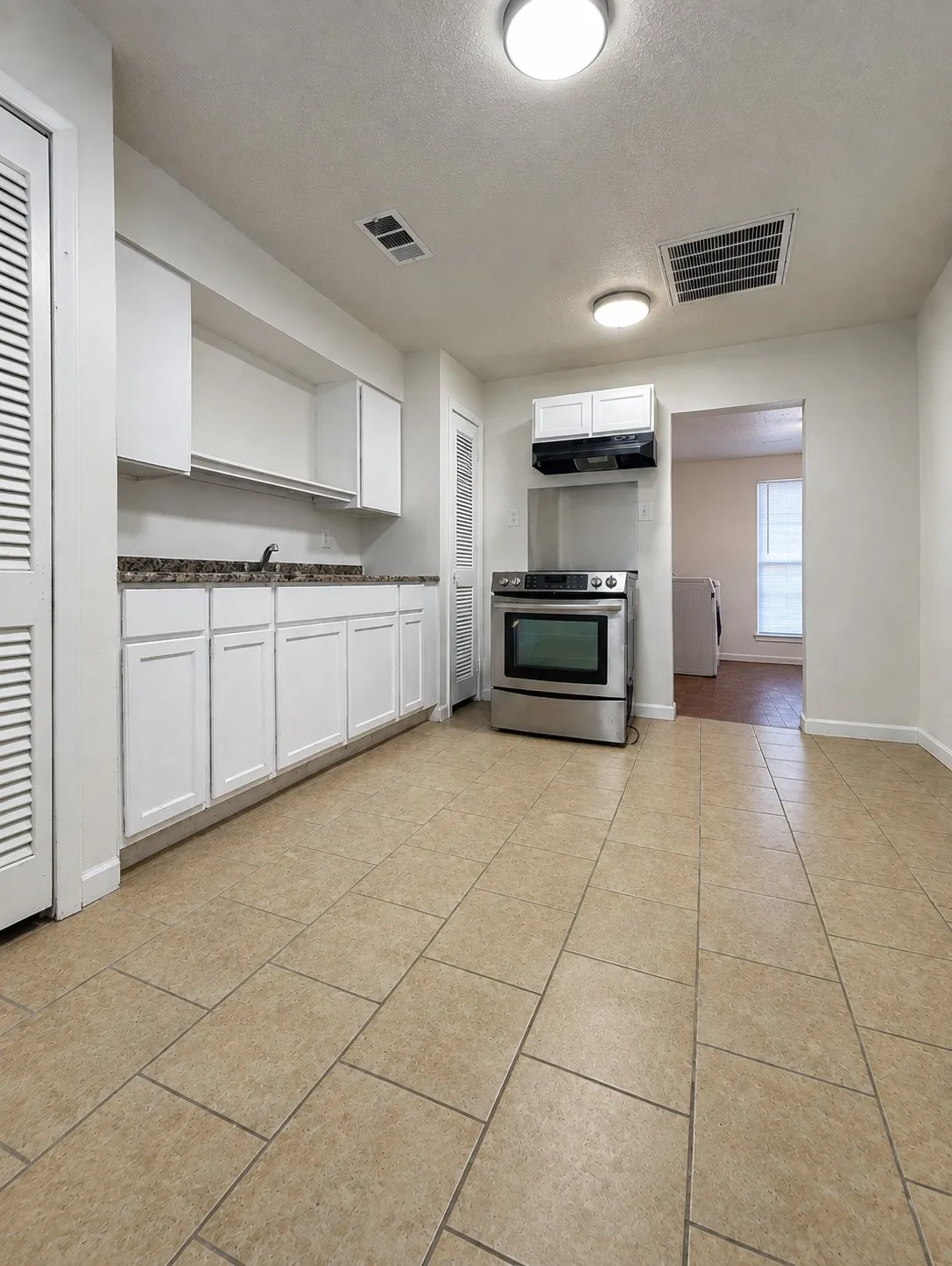 White cabinetry, stone-finish laminate countertops, stainless steel range, and neutral tile flooring