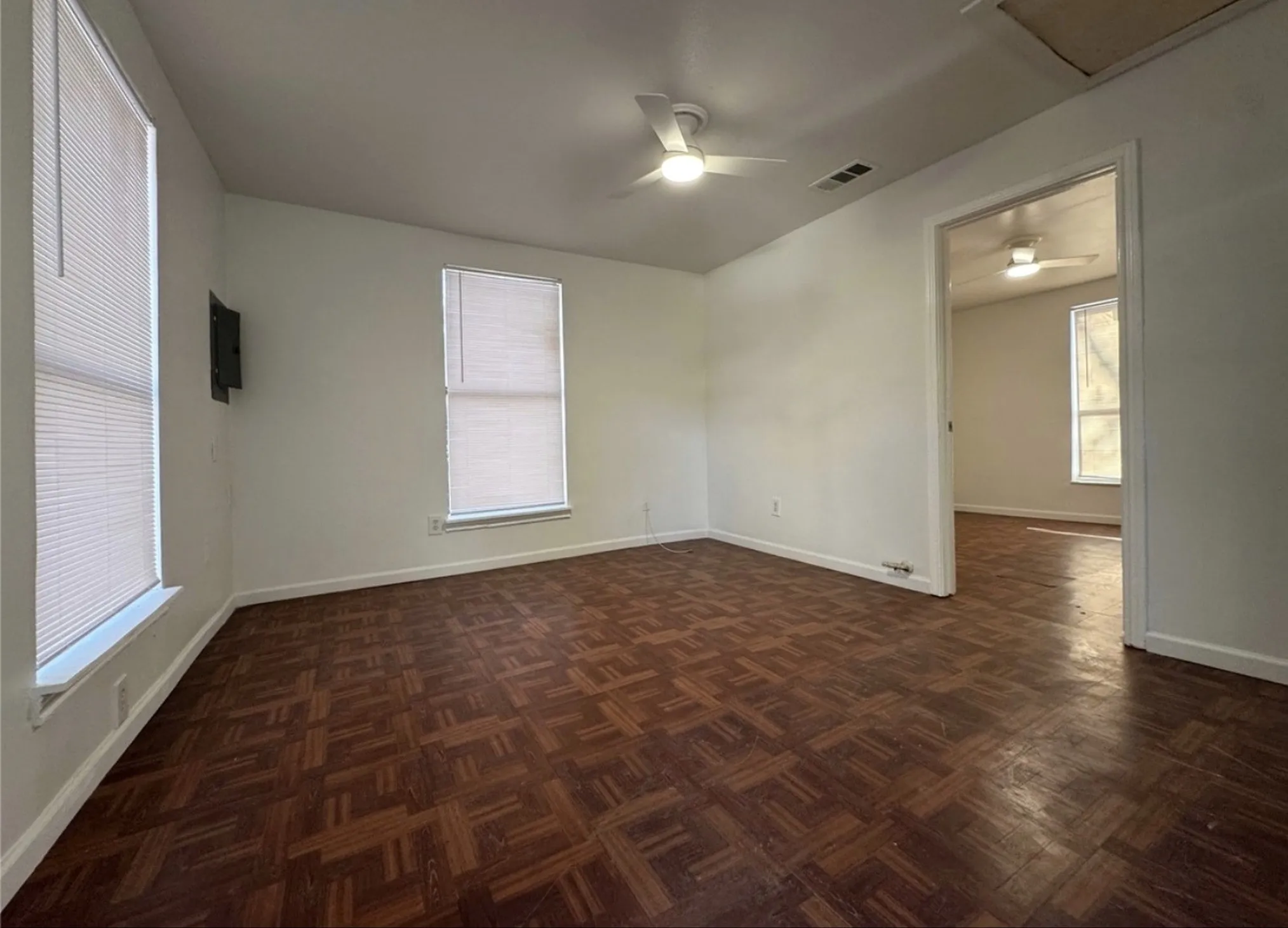 Parquet wood-finish flooring, white walls, two windows with blinds, and a ceiling fan with integrated lighting