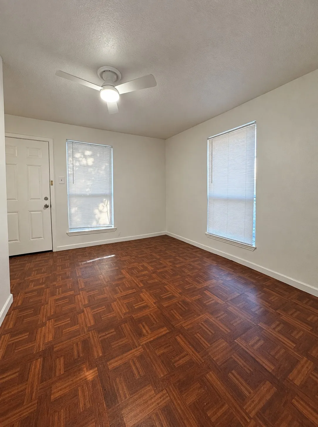 Parquet wood-finish flooring, white walls, and a ceiling fan with integrated lighting