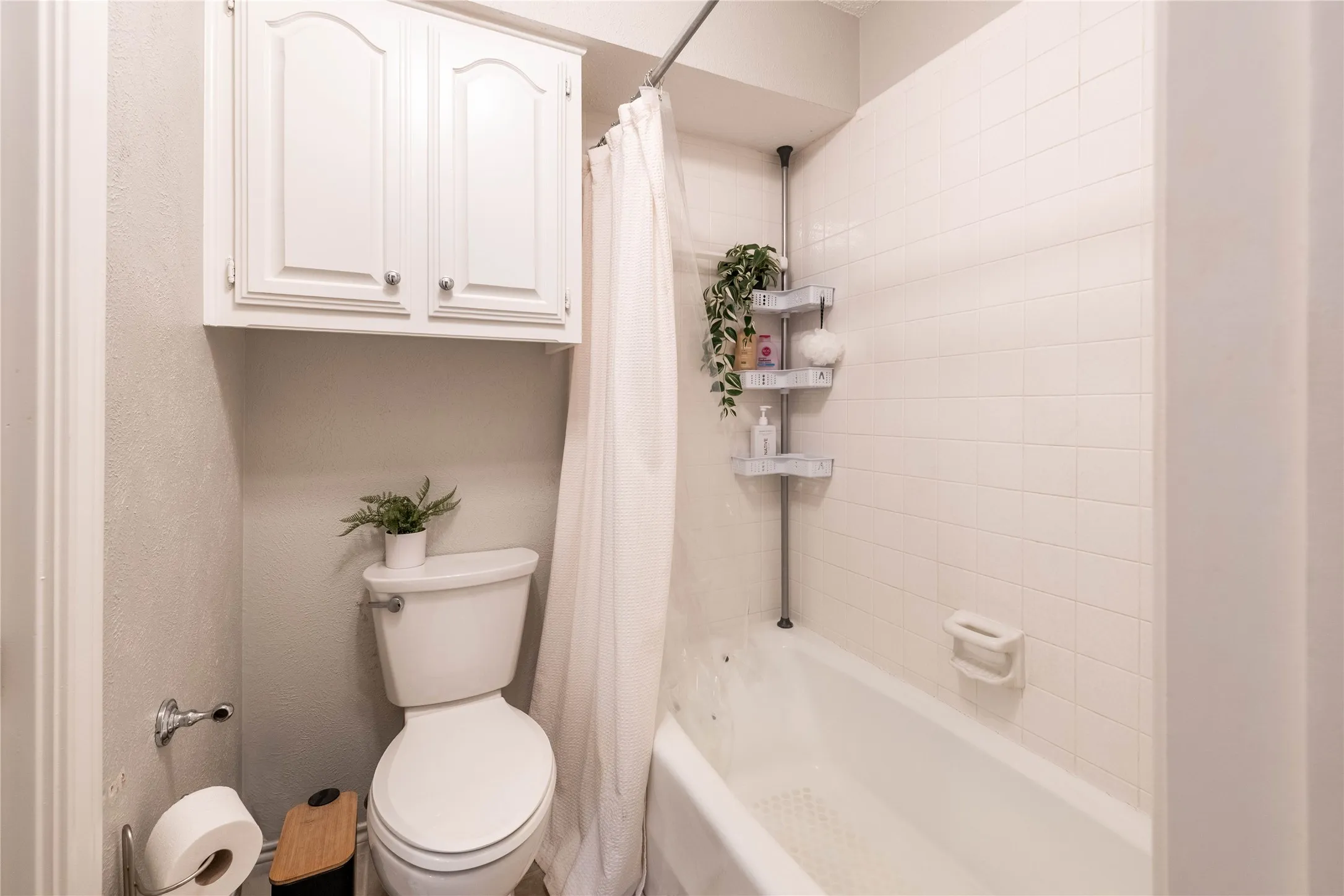 White overhead cabinetry, white toilet, white bathtub, and white wall tile