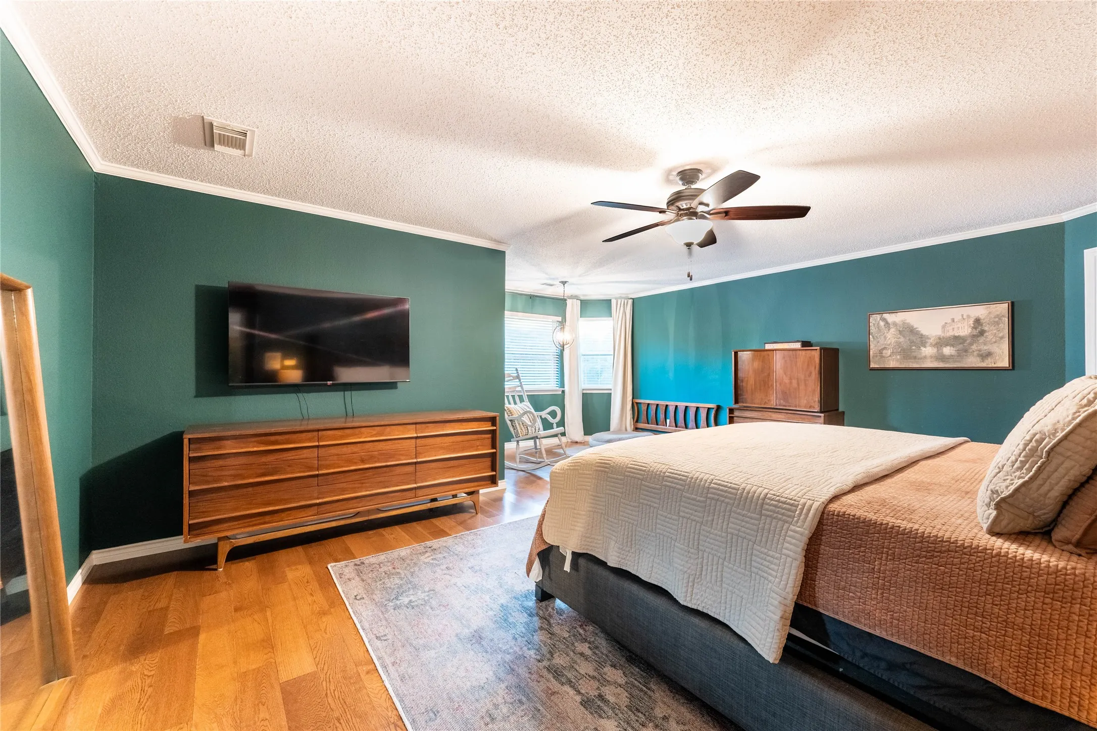 Hardwood-style flooring, ceiling fan, crown molding, multiple windows, and a mounted flat-screen television