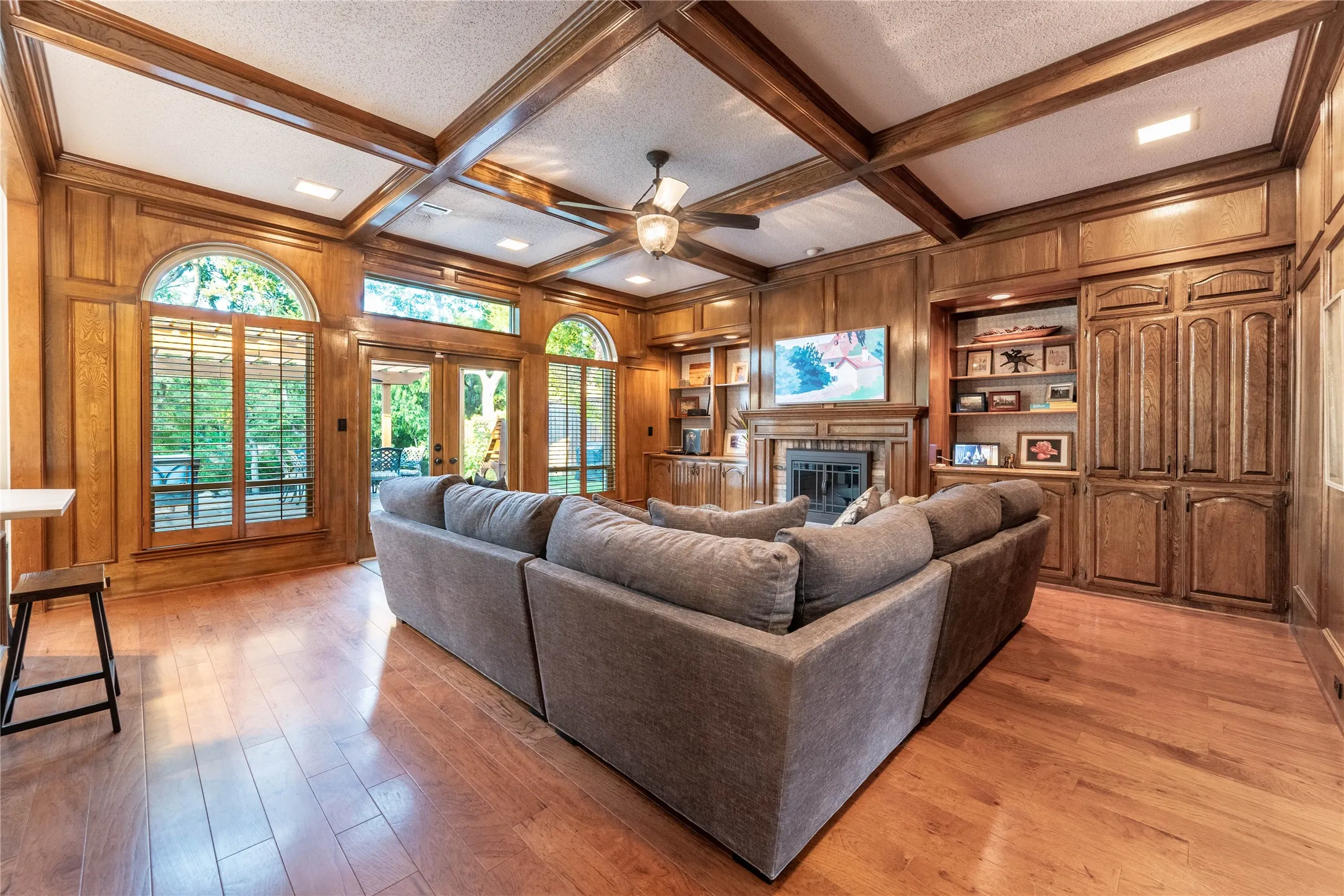 Hardwood flooring, wood paneling, coffered ceiling, built-in cabinetry, and a fireplace with a mantel