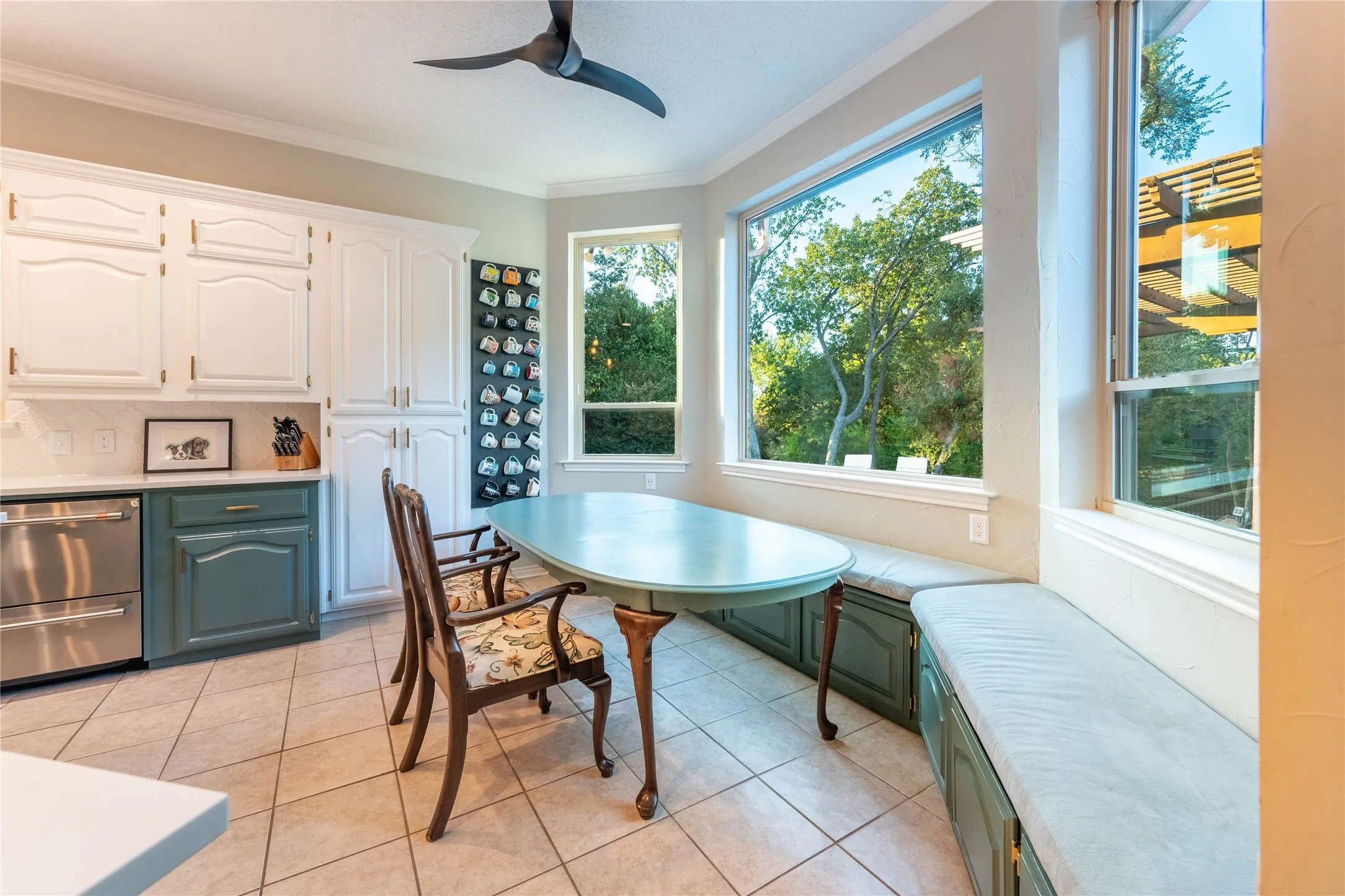 Bay window with built-in bench seating, white upper cabinetry, complementary lower cabinetry, stainless steel dishwasher, and tiled flooring