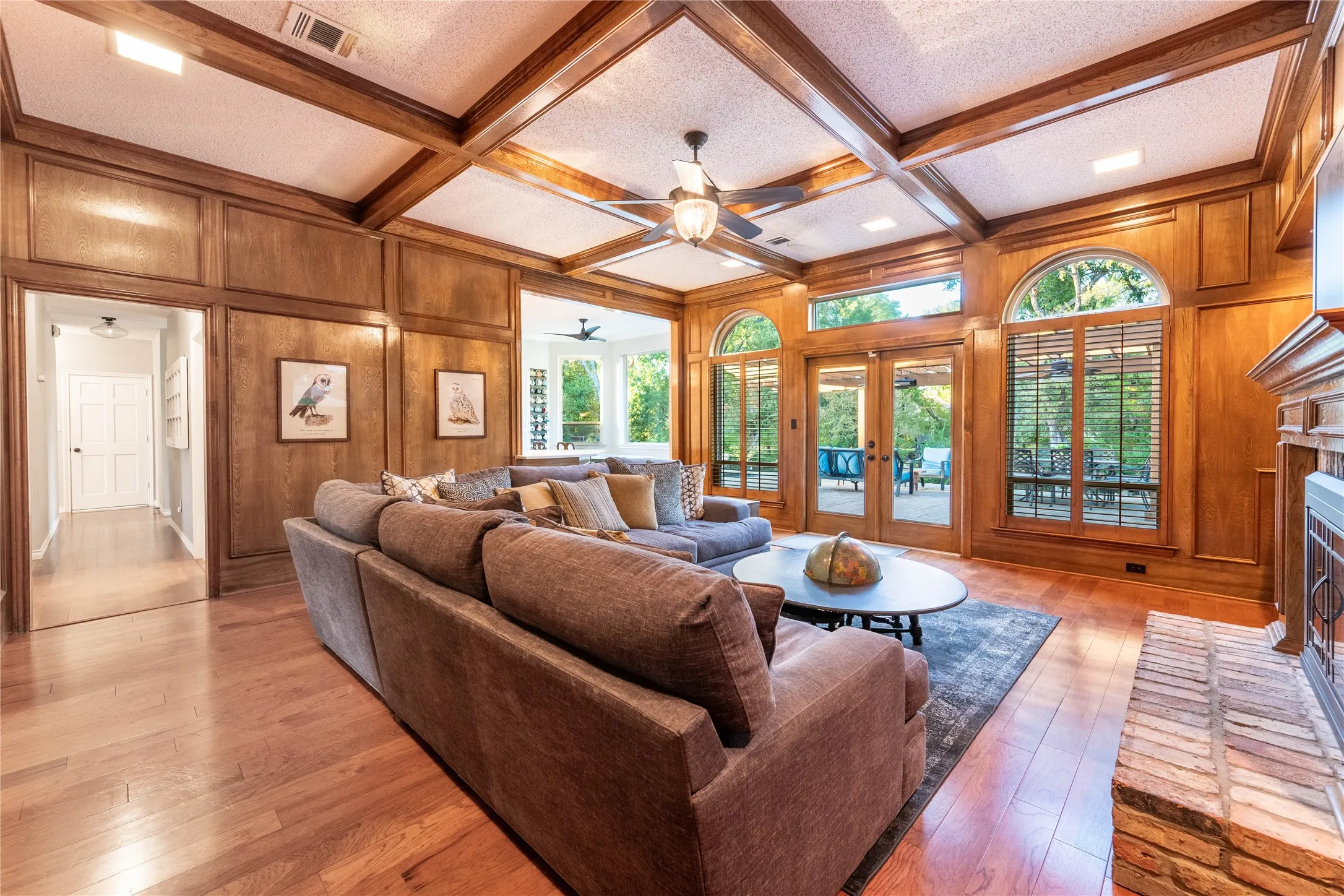Hardwood flooring, wood paneling, coffered ceiling, brick fireplace, and arched windows with french doors