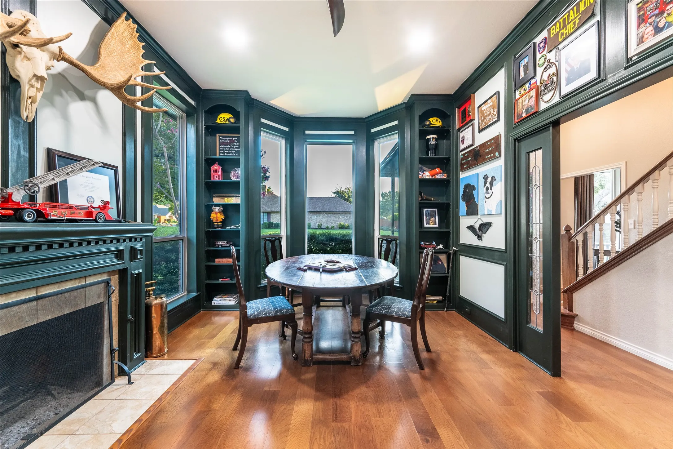 Hardwood flooring, built-in shelving, bay windows, fireplace with tile surround, and a glass-paneled door