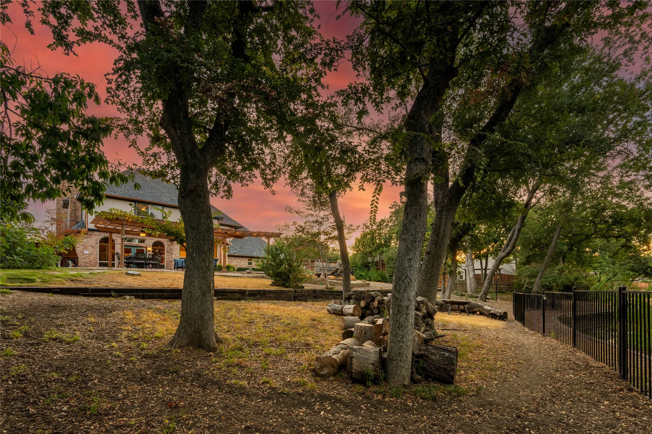 Expansive yard with mature trees, a multi-level terraced landscape, and a wrought iron fence