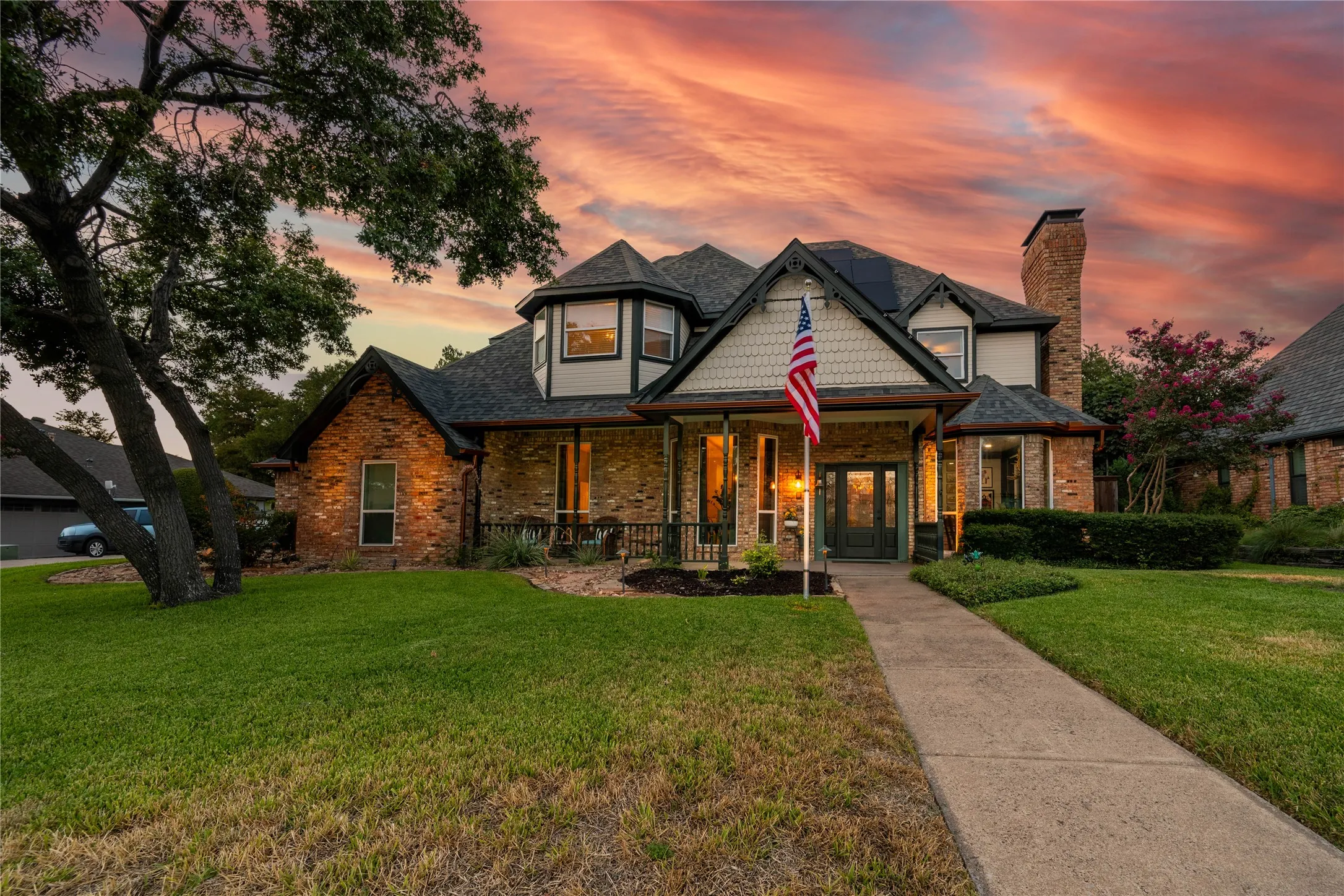 Brick exterior with mixed siding accents, mature landscaping, prominent front porch, and a concrete pathway