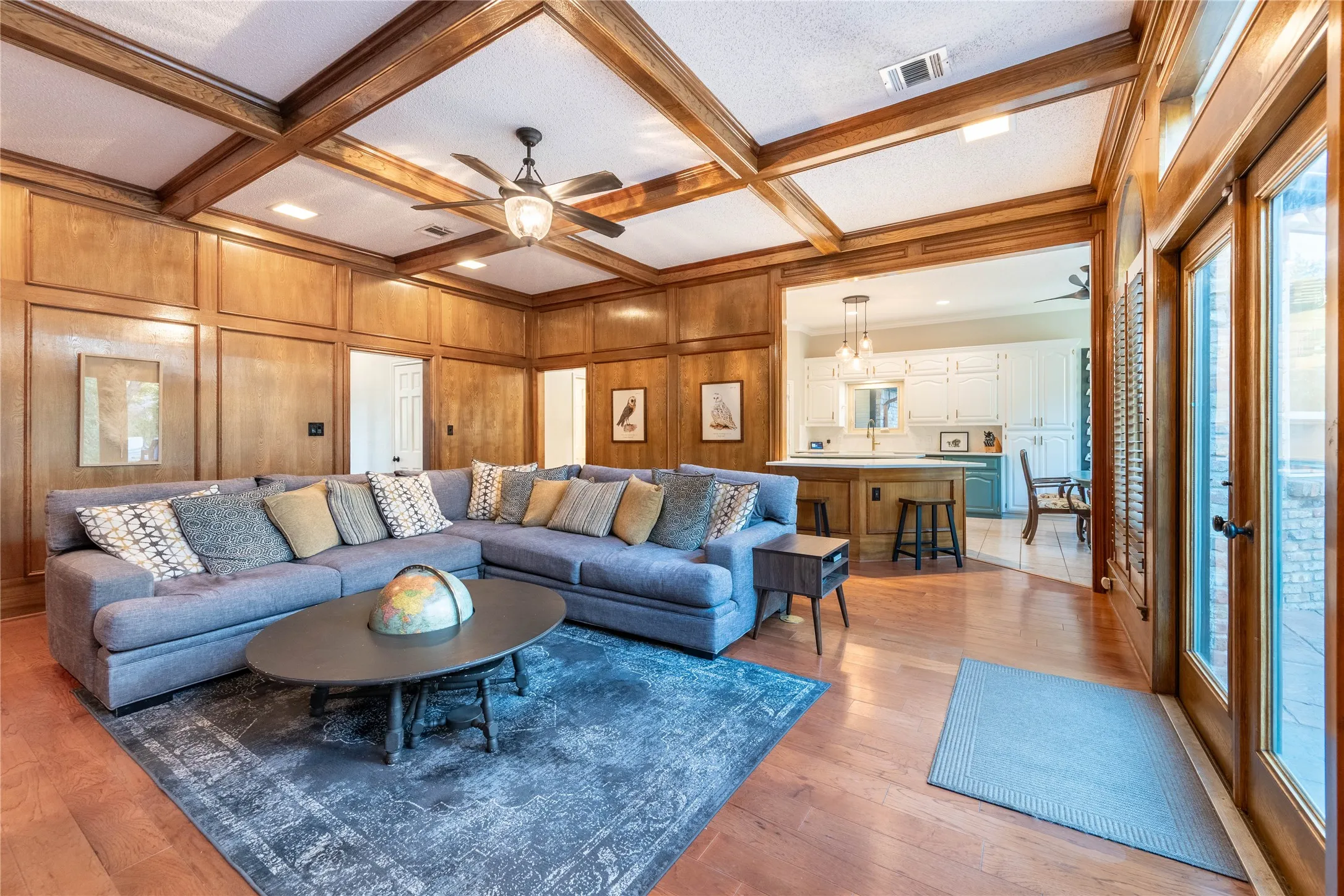 Wood-paneled walls with coffered ceiling, hardwood flooring, ceiling fan, and French doors