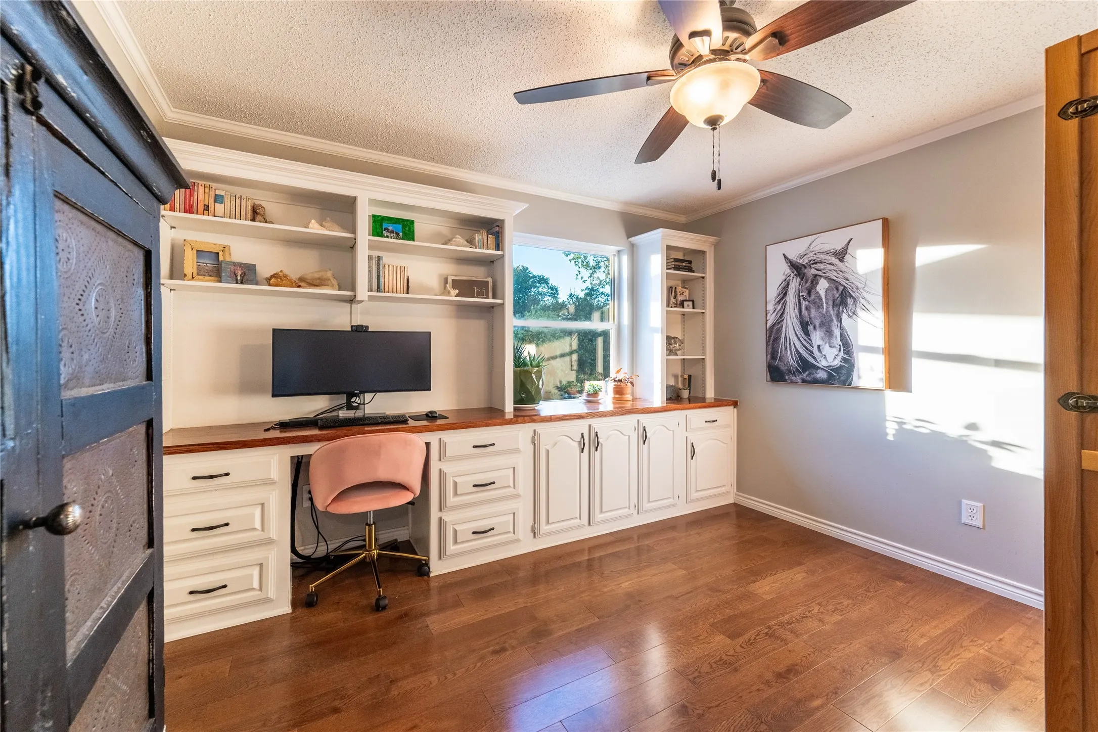 Wood-finish flooring, built-in cabinetry with a wood-finish countertop, recessed shelving, and a ceiling fan with integrated lighting