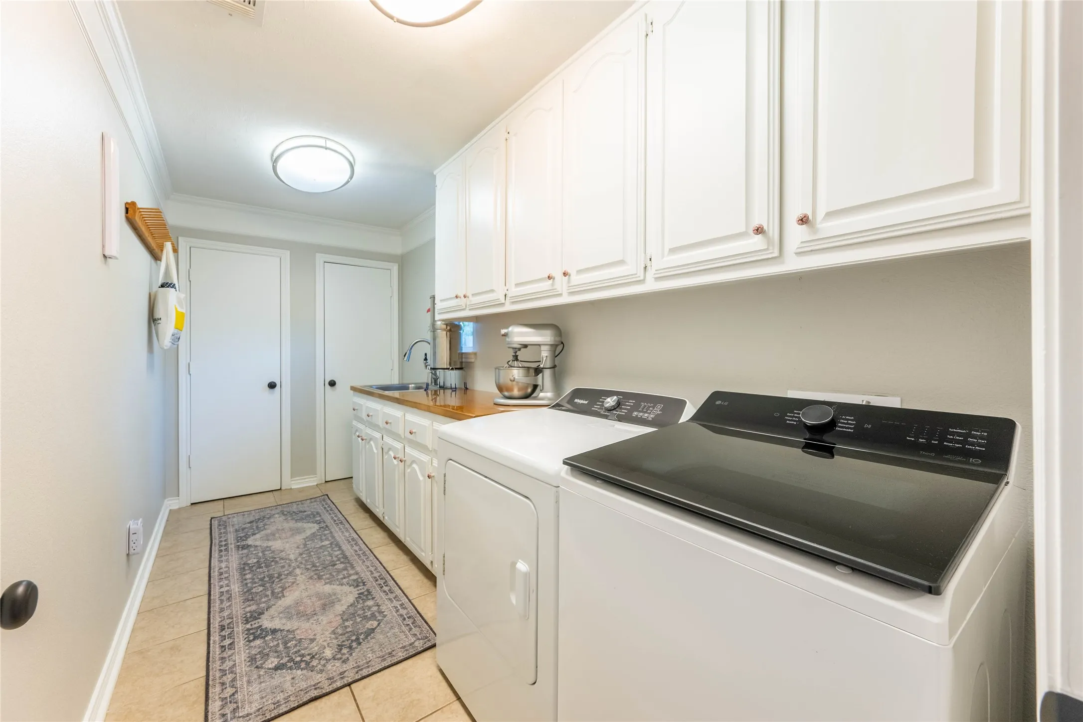 Laundry room featuring white cabinetry, wood-finish countertop, stainless steel sink, and tile flooring