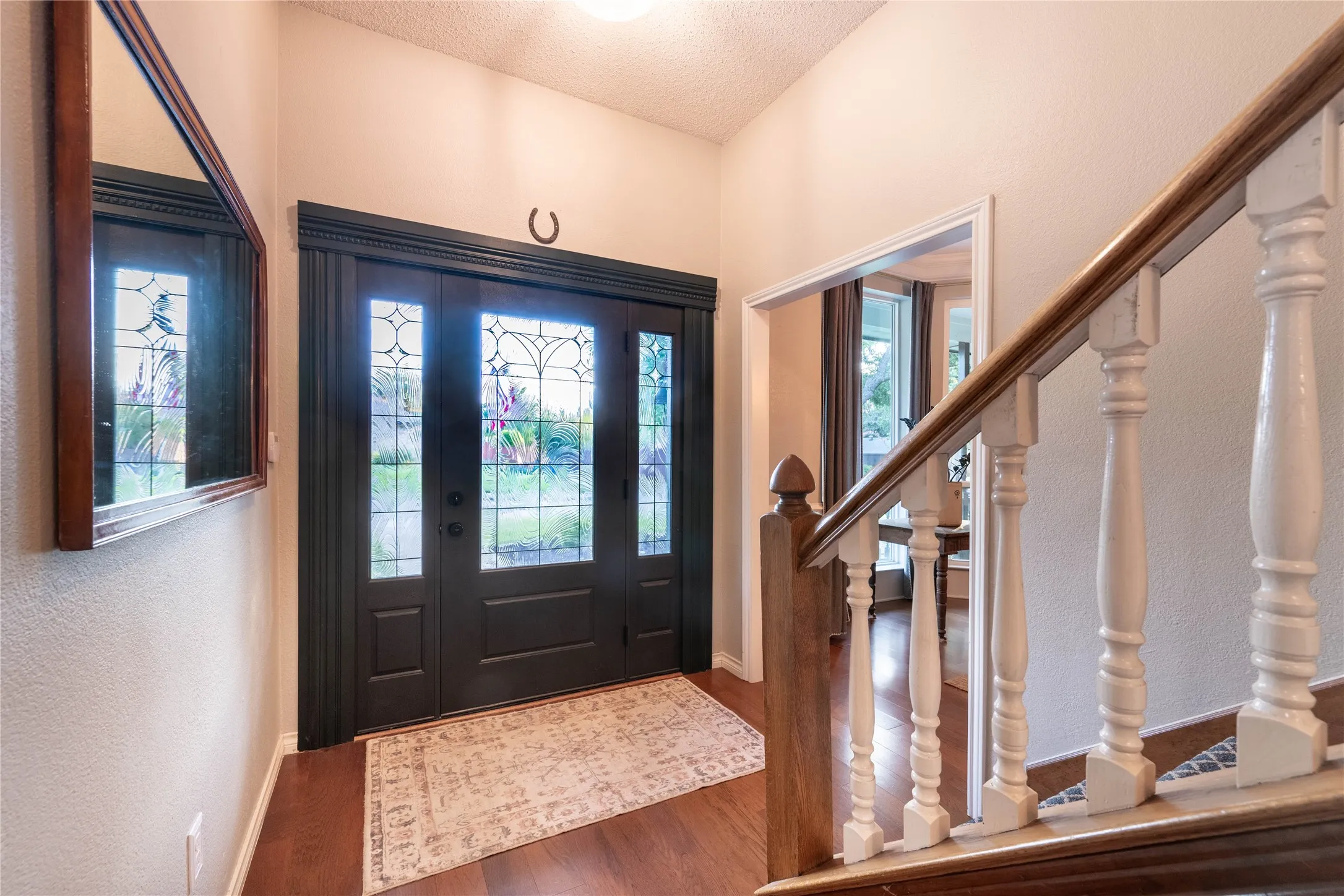 Entryway featuring wood-finish flooring, a dark-toned door with decorative glass panels, and a staircase with a wood handrail and white balusters