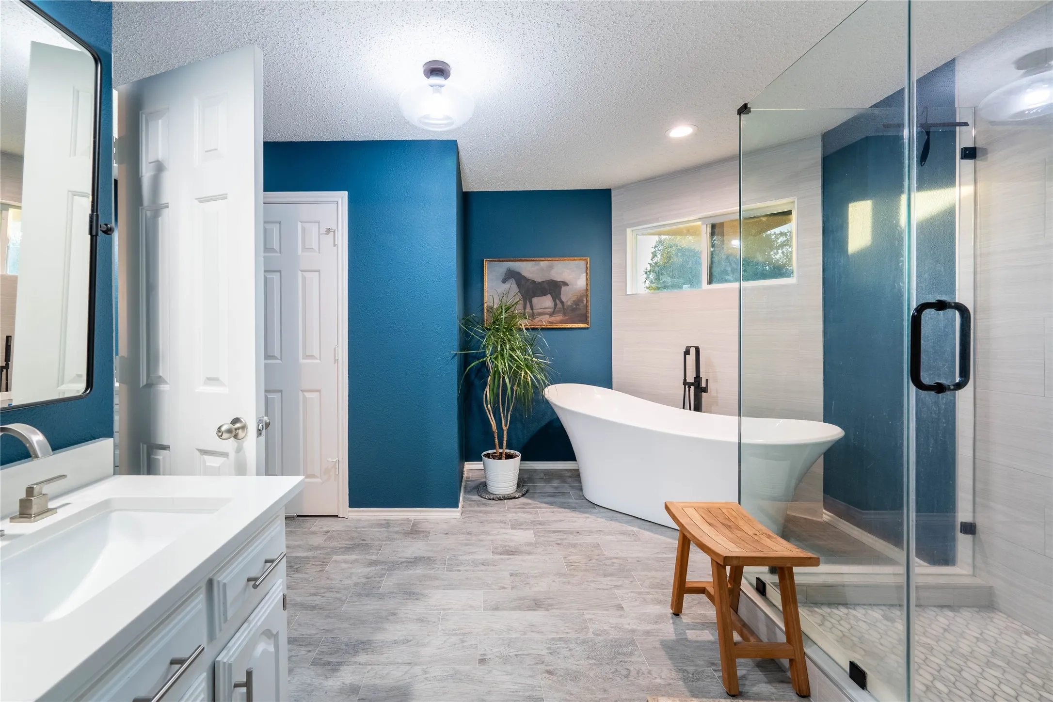 Contemporary bathroom featuring a freestanding soaking tub, clear glass shower enclosure, wood-finish flooring, and a vanity with an integrated sink