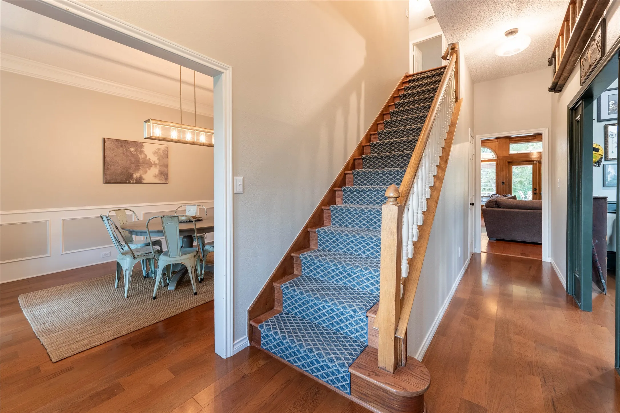 Hardwood flooring, painted walls, wainscoting, staircase with wood banister, and overhead lighting fixtures