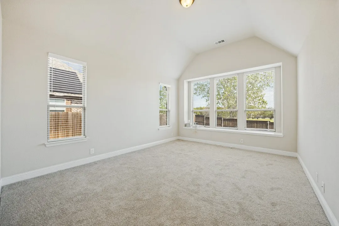Bright corner room with expansive multi-pane windows overlooking mature landscaping, neutral carpet flooring, and soft recessed lighting